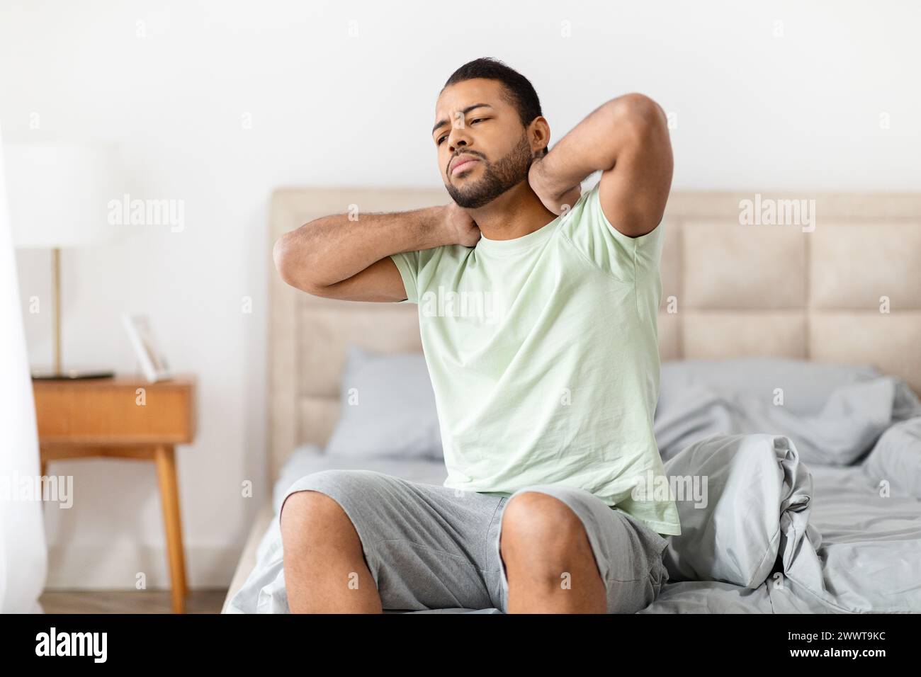 Mann mit Nackenschmerzen, der auf der Bettkante sitzt Stockfoto