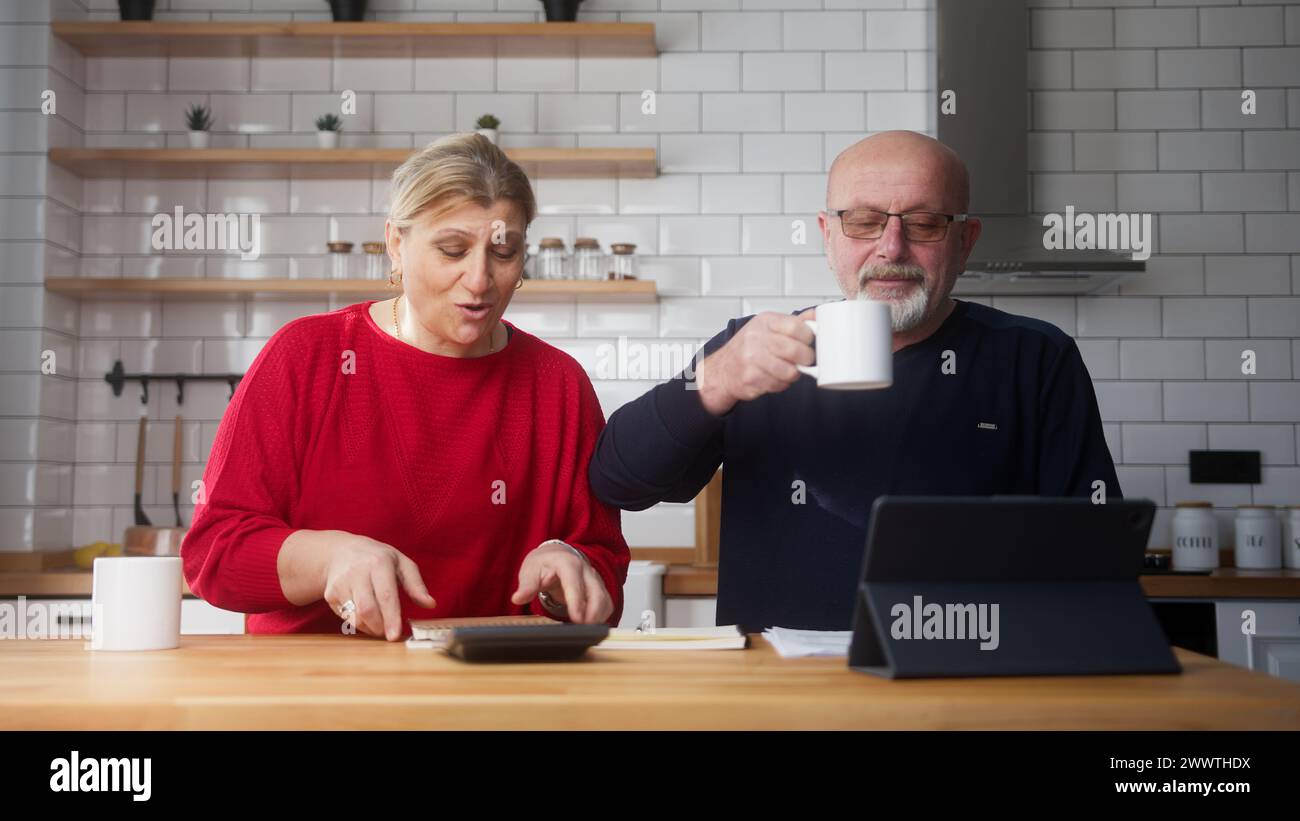 Altes Paar sitzt in der Küche und macht Papiere, überprüft Rechnungen, Bankkreditzahlungen, diskutiert unbezahlte Steuern. Alte Großeltern Familiengeld Prob Stockfoto