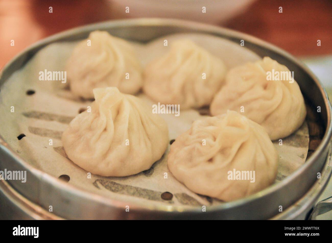 Nahaufnahme des gedämpften chinesischen Xiao Long Tang Bao, auch bekannt als Suppenknödel, weil die Füllung darin tatsächlich flüssige Suppe ist, die aus braunem Holz serviert wird Stockfoto