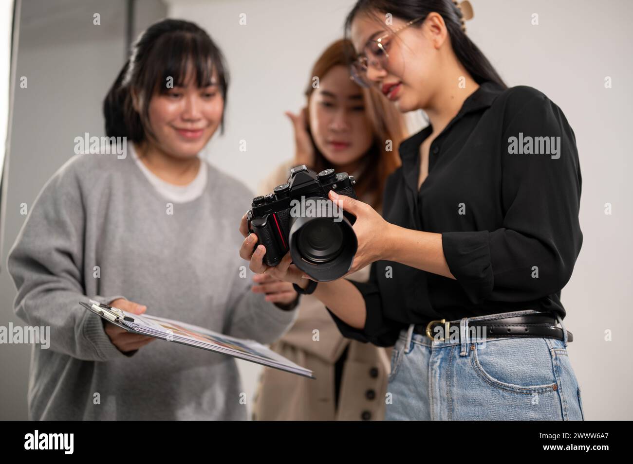 Eine professionelle asiatische Fotografin zeigt Bilder auf ihrer Kamera an Art Directors und arbeitet mit ihrem Team im Studio mit professionellem Licht Stockfoto