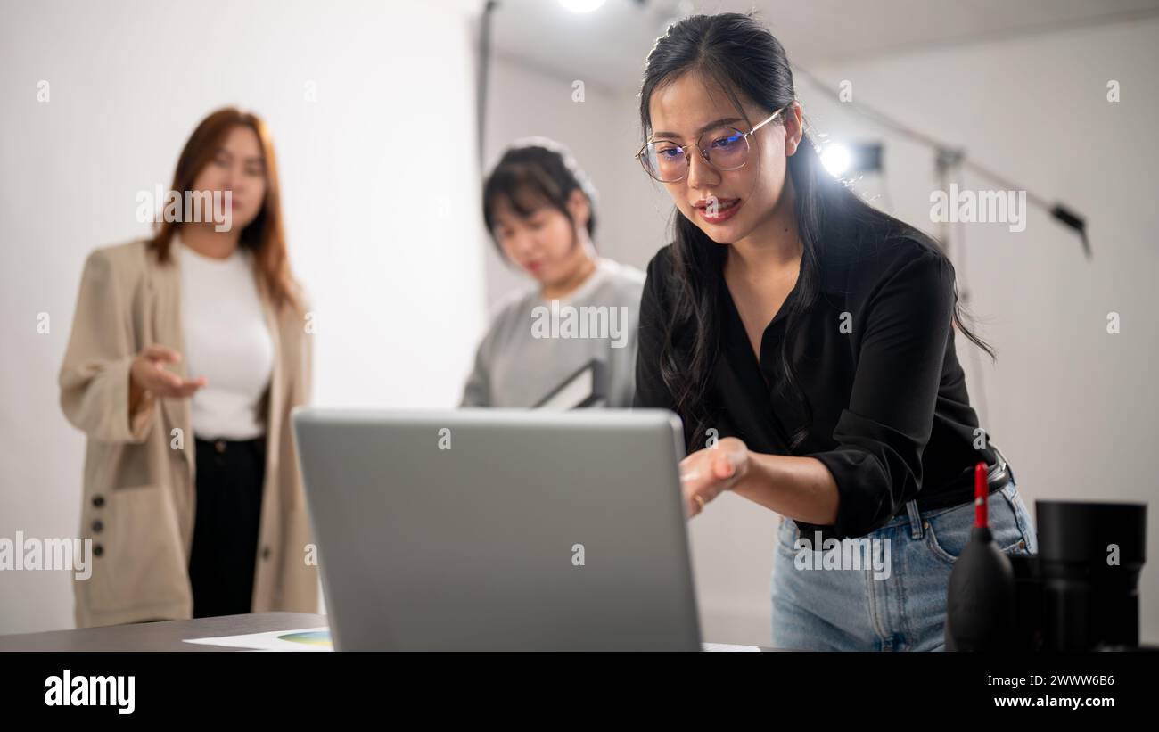 Eine erfahrene asiatische Fotografin überprüft Bilder auf ihrem Laptop, informiert das Konzept, bereitet sich auf ein Fotoshooting vor und arbeitet im Studio Stockfoto