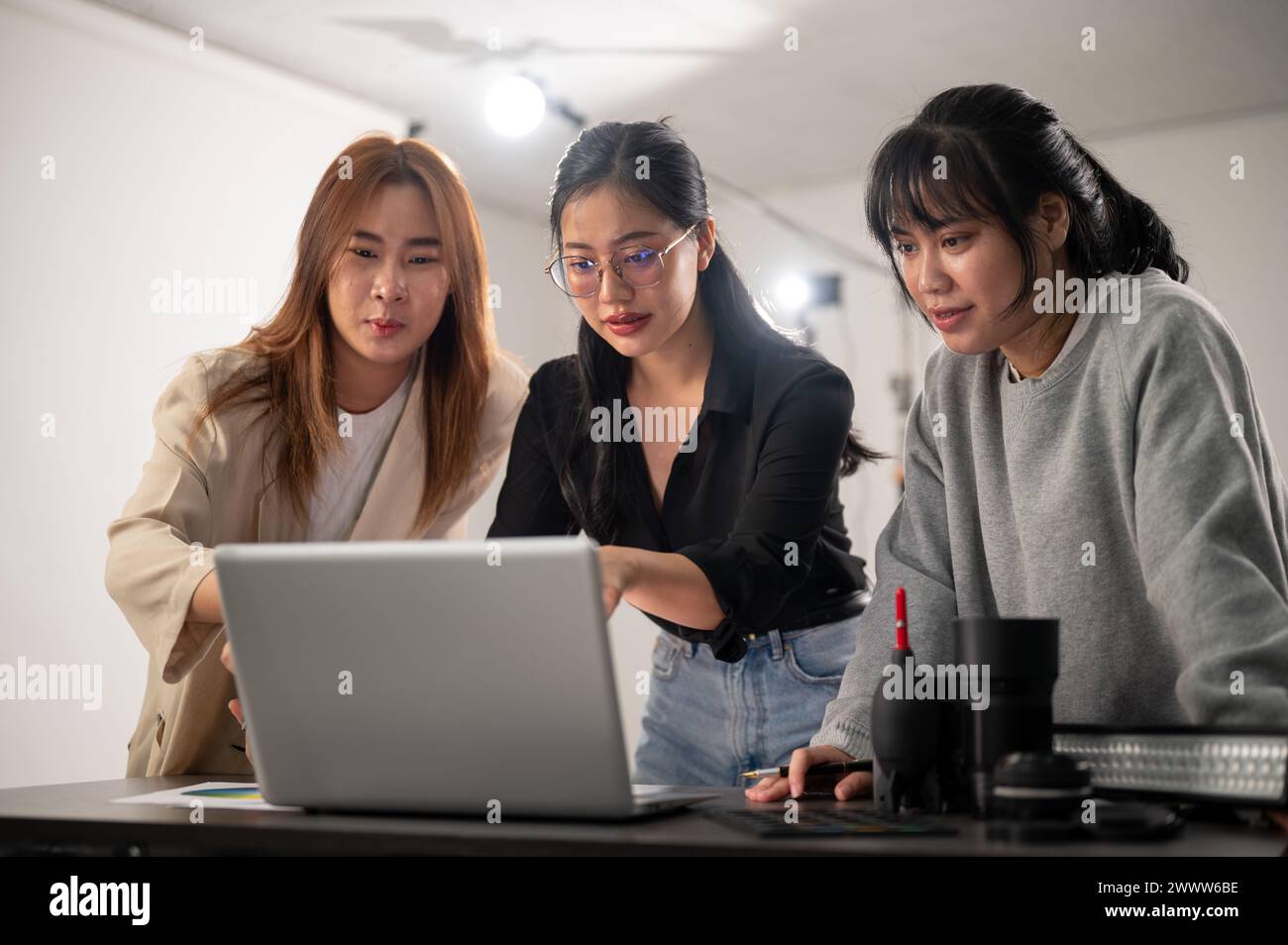 Eine erfahrene asiatische Fotografin überprüft Bilder auf ihrem Laptop, informiert das Konzept, bereitet sich auf ein Fotoshooting vor und arbeitet im Studio Stockfoto