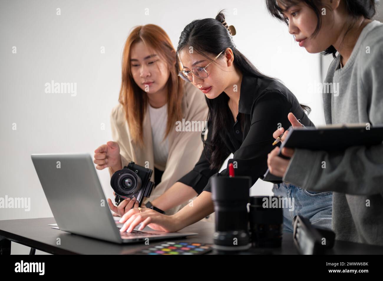 Eine professionelle asiatische Fotografin arbeitet mit ihren Assistenten in einem Fotoshootingstudio, spricht, informiert über das Konzept, überprüft Bilder auf dem Stockfoto