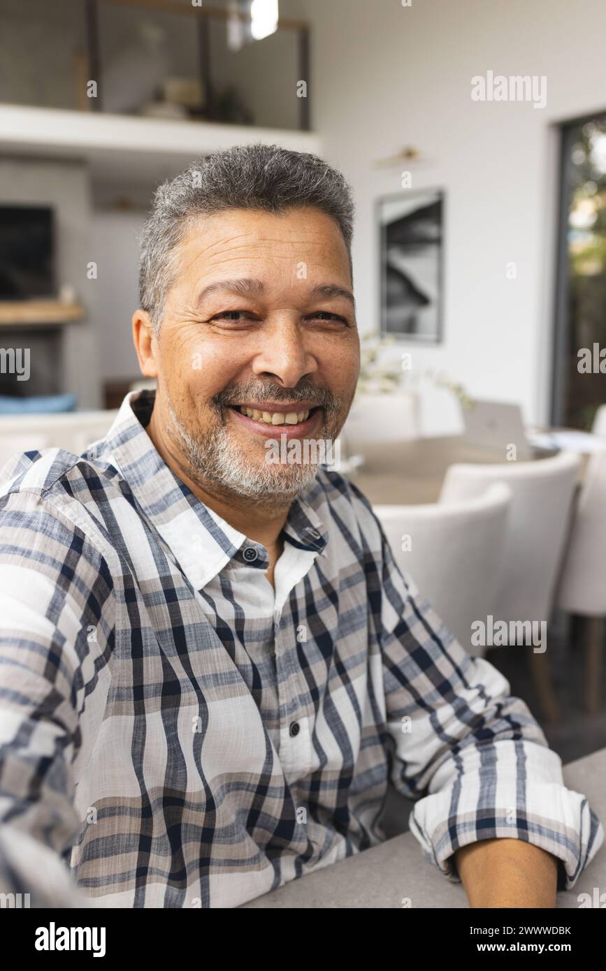 Ein älterer birassischer Mann lächelt herzlich, sitzt drinnen zu Hause Stockfoto