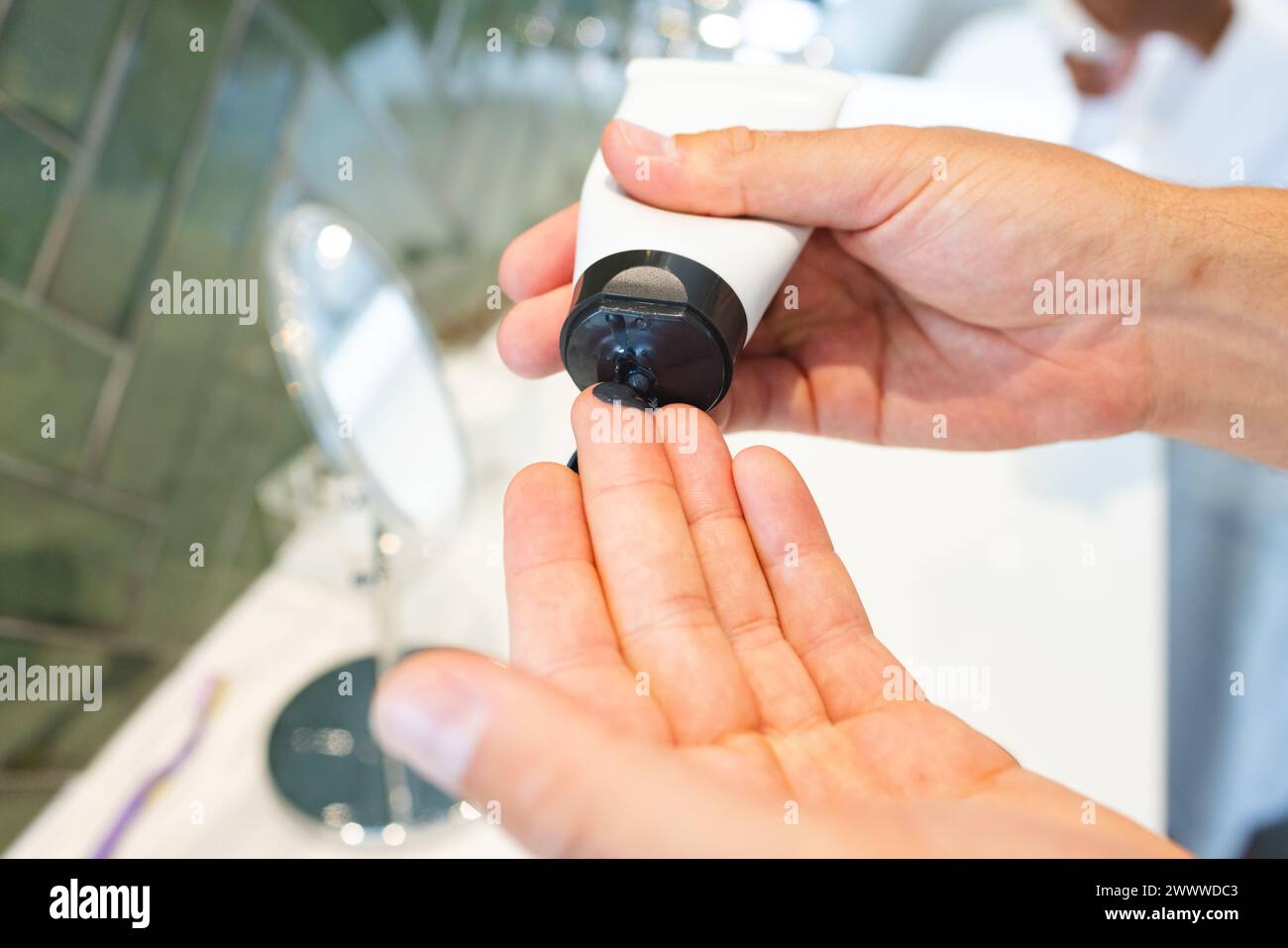 Eine Person spendet Gesichtsreiniger aus einer Flasche auf ihre Hand im Badezimmer Stockfoto