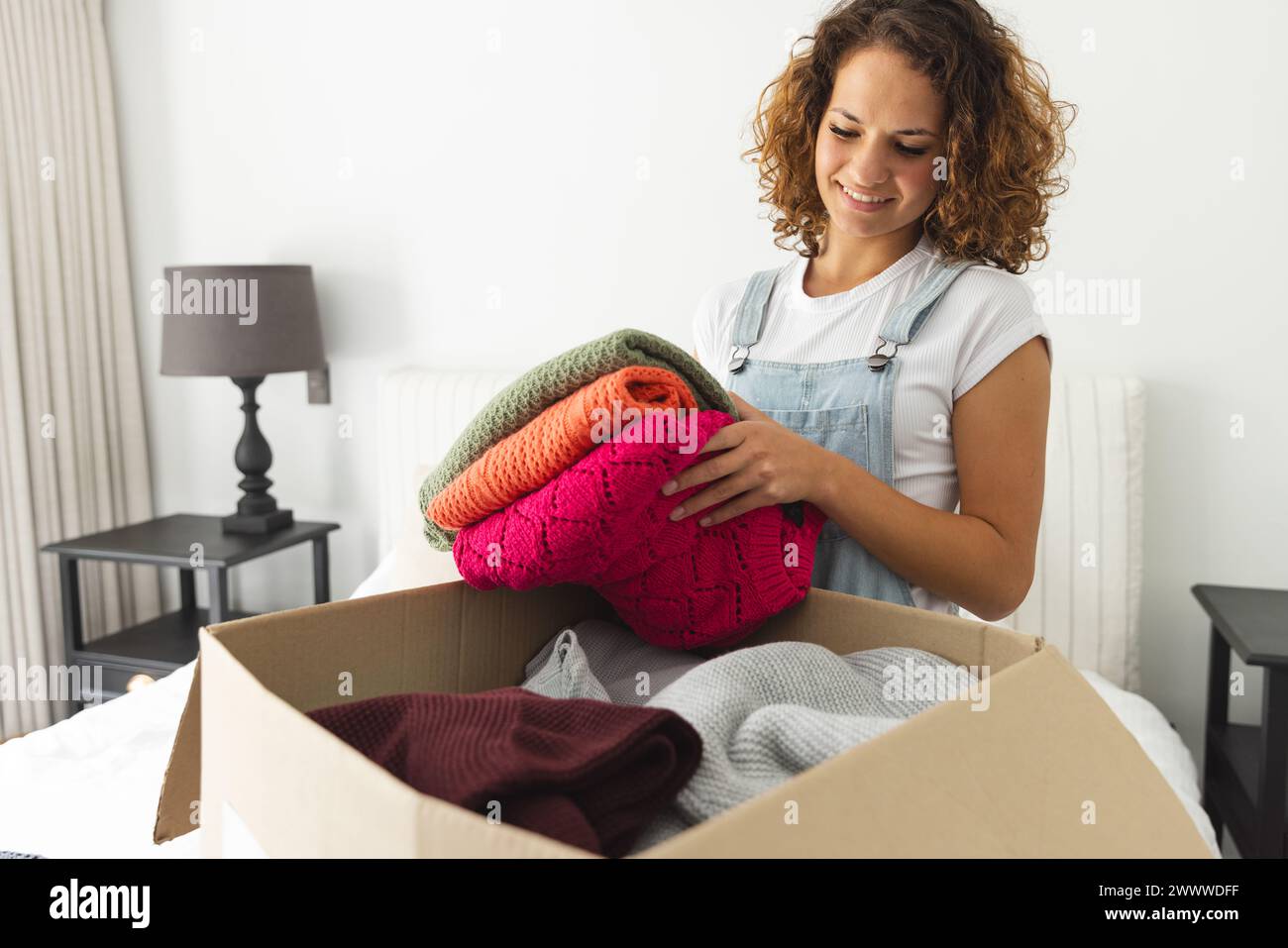 Eine junge Kaukasierin packt bunte Pullover aus einer Schachtel und sortiert Kleidung für Spenden Stockfoto
