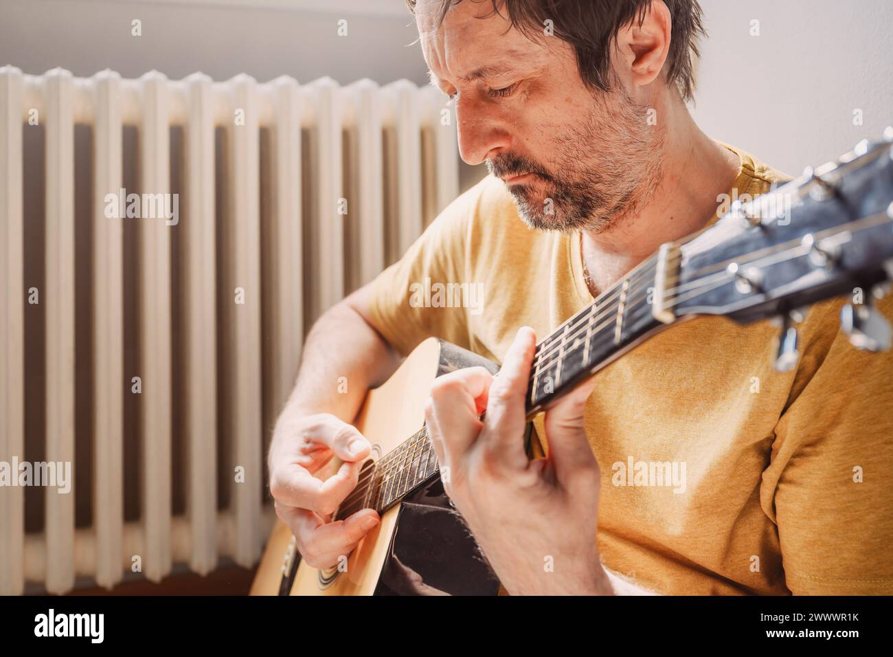 Einsamer Mann im mittleren Erwachsenenalter, der zu Hause Akustikgitarre spielt, selektiver Fokus Stockfoto