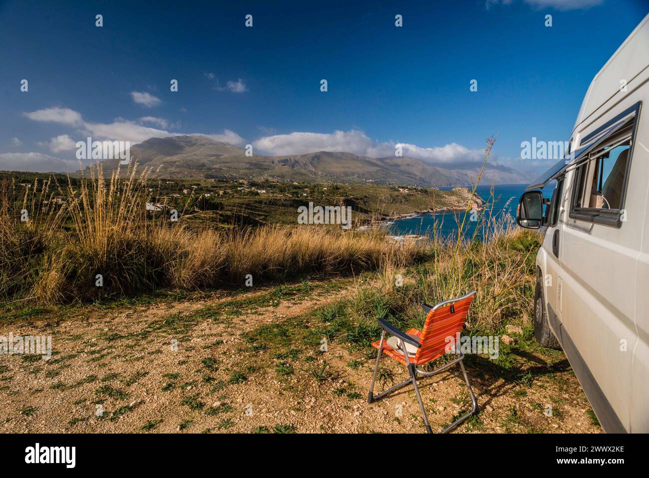 Ein Campingbus vor dem ein Campiingstuhl steht auf einem unbefestigten Offroad Stellplatz an der Küste am Mittelmeer auf Sizilien, Italien. Ein Wohnmobil steht auf einem Stellplatz am Ufer des Mittelmeers. *** Ein Wohnmobil vor einem Campingstuhl steht auf einem unbefestigten Off-Road-Platz an der Mittelmeerküste in Sizilien, Italien Ein Wohnmobil steht auf einem Stellplatz am Ufer des Mittelmeers Stockfoto