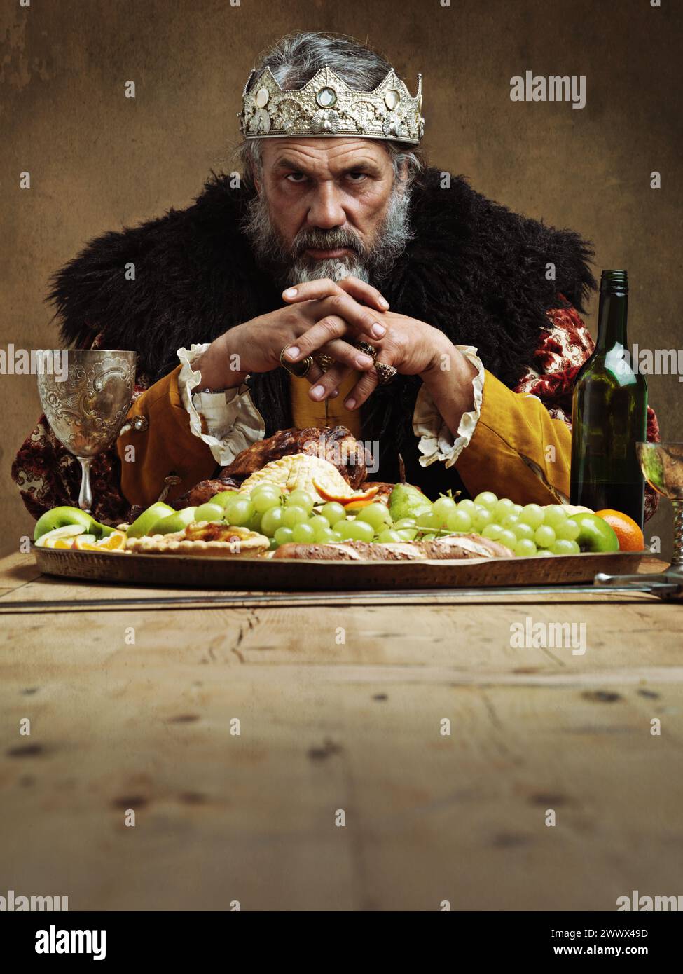 König, Essen und Porträt im Bankettsaal auf dem Tisch zum Festessen mit Wein und Obst zum Essen und Trinken. Reife Person oder Mann mit Krone für Könige und Stockfoto