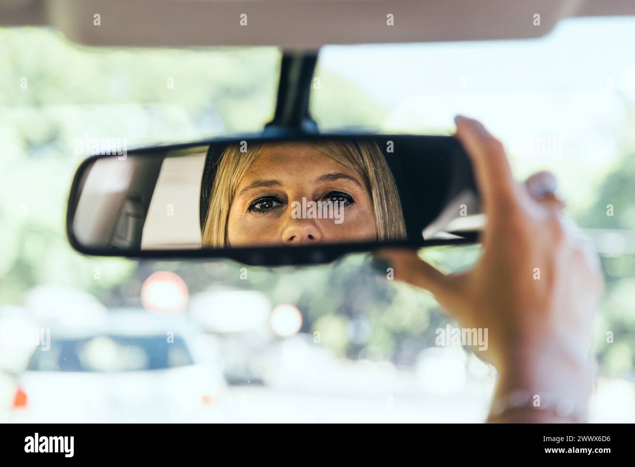 Fahrerin, die den Rückspiegel ihres Autos einstellt. Stockfoto
