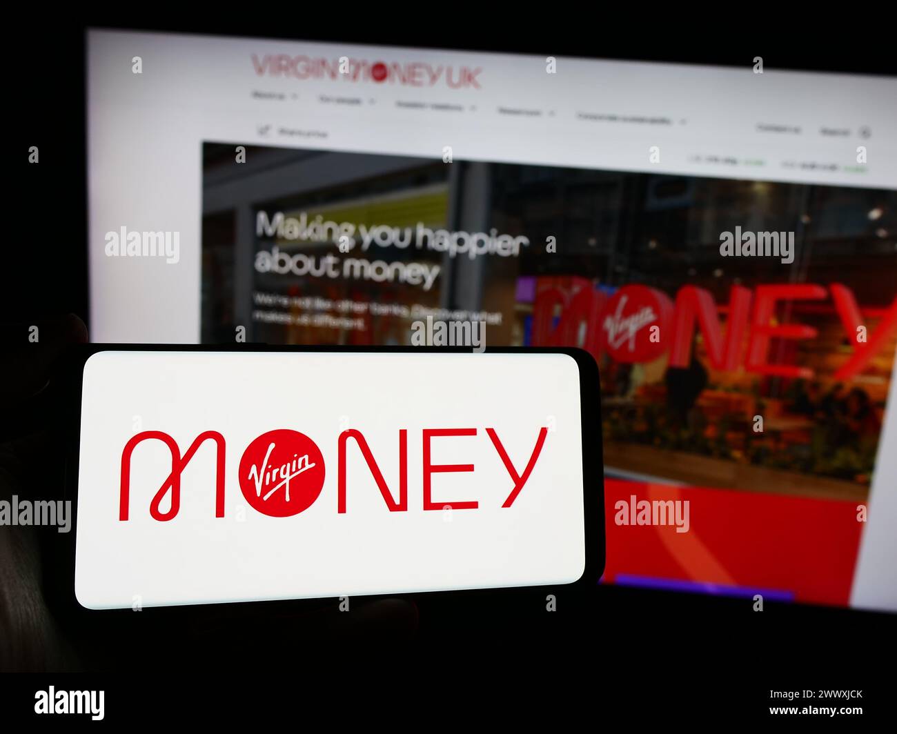 Person mit Smartphone und Logo des britischen Finanzdienstleisters Virgin Money vor der Website. Schwerpunkt auf dem Display des Telefons. Stockfoto