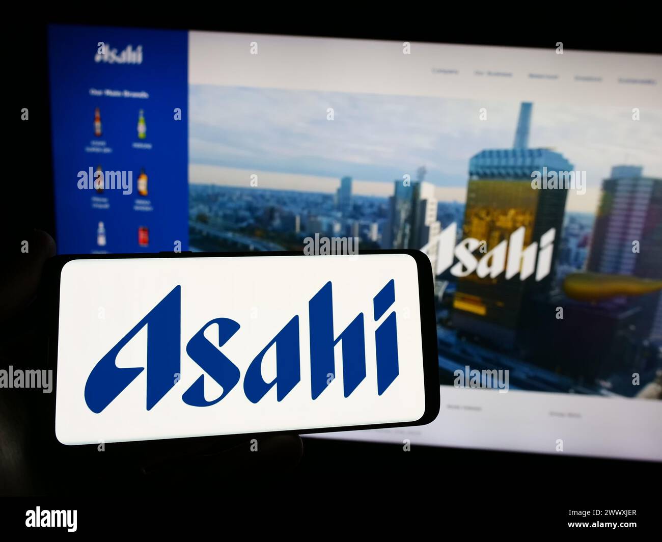 Person mit Smartphone und Logo des japanischen Brauunternehmens Asahi Group Holdings Ltd. Vor der Website. Schwerpunkt auf dem Display des Telefons. Stockfoto