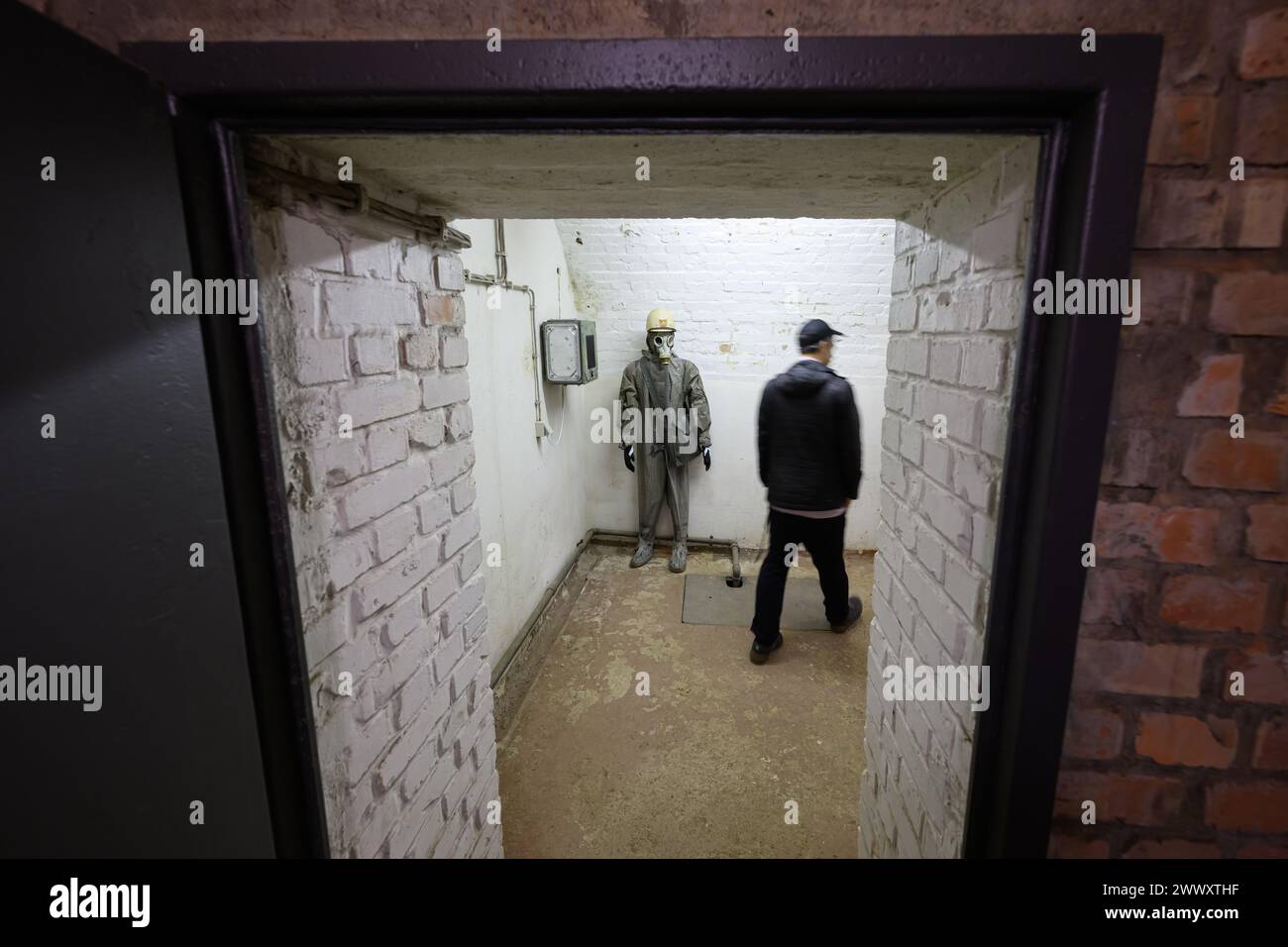 26. März 2024, Sachsen, Königstein: Ein Teilnehmer der Pressetour der neuen Ausstellung „Kernbunker und Pulvermagazin“ geht in einem ehemaligen Bunker für den DDR-Zivilschutz auf der Festung Königstein an einer Schaufensterpuppe mit Schutzanzug und Gasmaske vorbei. Die Festung Königstein macht Räume des einst geheimen DDR-Bunkers im Festungswald, die in der Ausstellung selten zu sehen sind, im Rahmen von Führungen zugänglich. Foto: Robert Michael/dpa Stockfoto