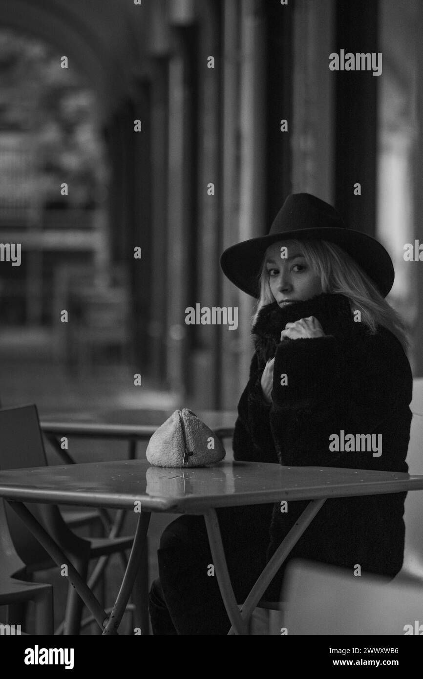 Frau mit schwarzem Hut und Pelzmantel an einem Café-Tisch in Schwarz-weiß-Ton, draußen, Winter Stockfoto