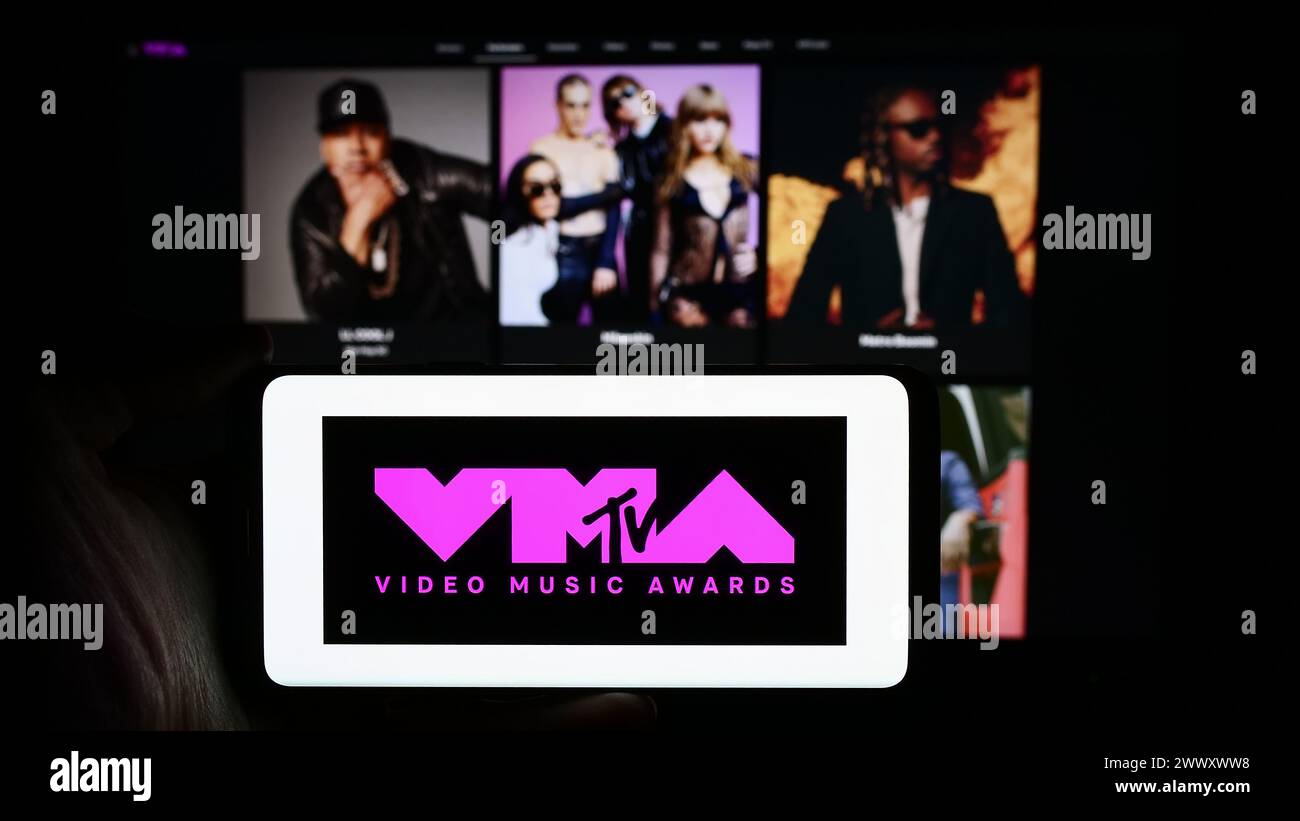 Person, die ein Mobiltelefon mit dem Logo der Preisverleihung MTV Video Music Awards (VMA) vor der Webseite des Unternehmens hält. Schwerpunkt auf dem Display des Telefons. Stockfoto