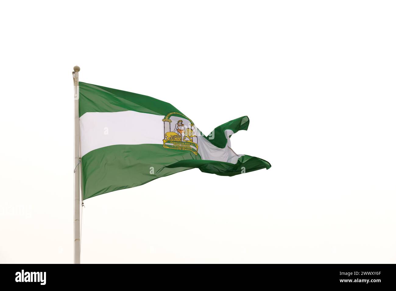 Die grün-weiße andalusische Flagge mit dem Emblem des Herkules und zwei Löwen wird gefangen, während sie unter dem hellen Mittag im Wind weht Stockfoto
