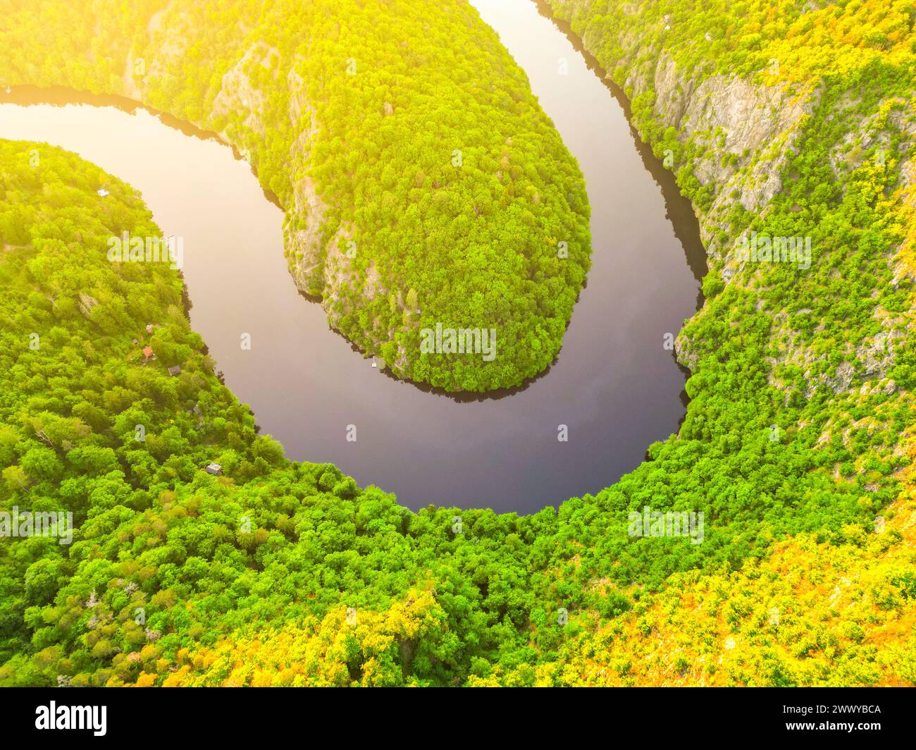 Ein Blick aus der Vogelperspektive auf einen ruhigen, gewundenen Fluss, der während der goldenen Stunde von üppigem Grün umgeben ist und die unberührte Schönheit der Natur zeigt. Stockfoto