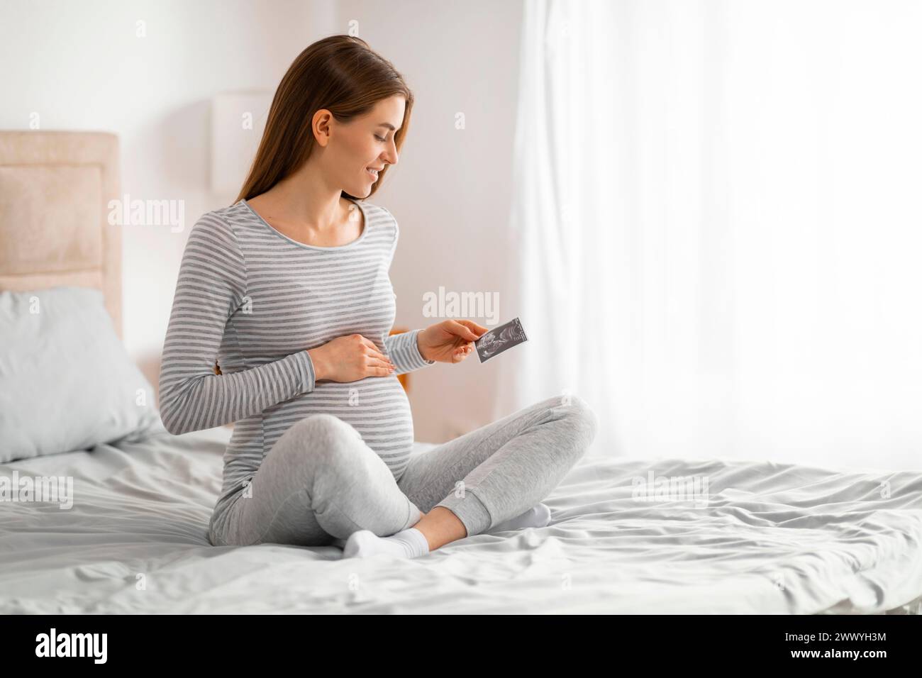 Schwangere Frau, die mit Ultraschall auf dem Bett sitzt Stockfoto