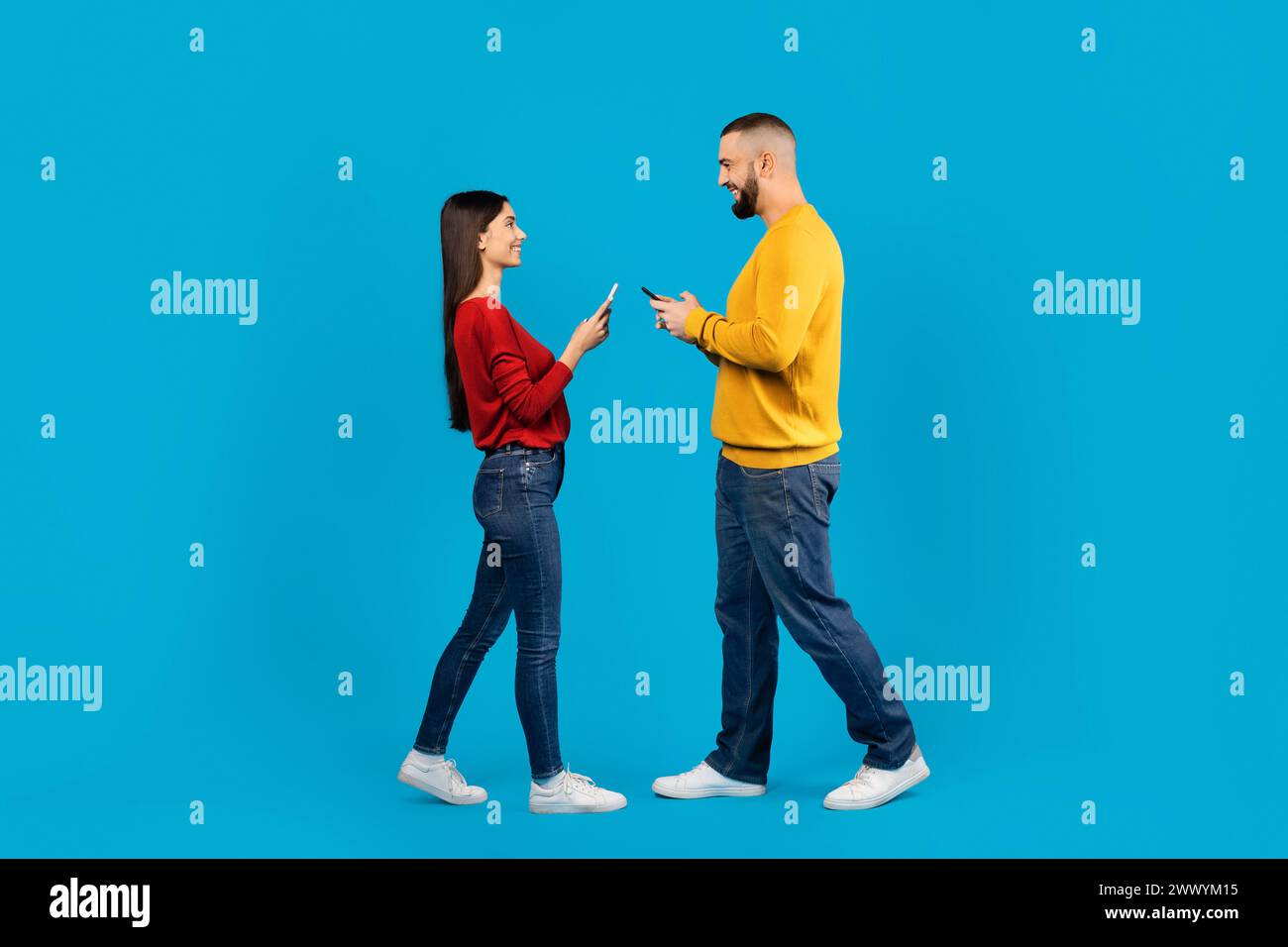 Fröhliches junges Paar, das von Angesicht zu Angesicht steht und jedes in sein eigenes Smartphone vertieft ist Stockfoto