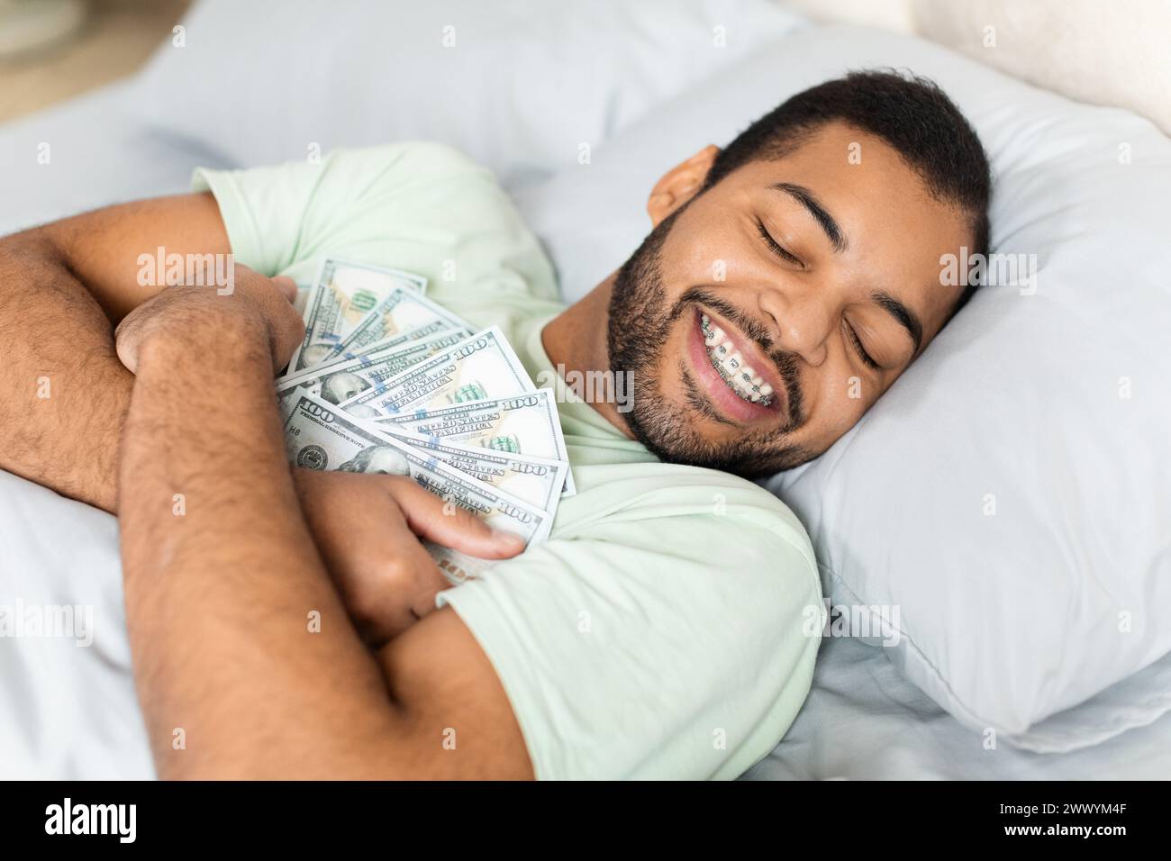 Mann umarmt Bargeld im Bett, was auf Reichtum hindeutet Stockfoto