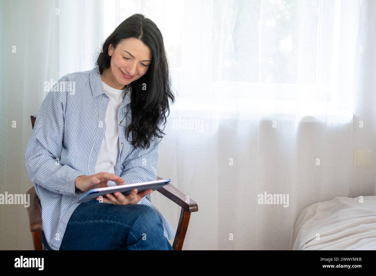 Content Midlife-Frau, die sich lässig kleidet, in einem digitalen Tablet vertieft ist und moderne Konnektivität und lebenslanges Lernen verkörpert. Hochwertige Fotos Stockfoto
