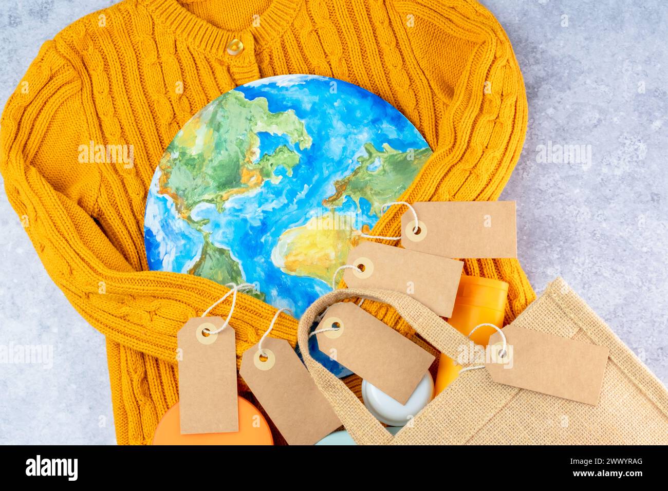 Die Pullover-Ärmel in Gelb halten die Umarmung des Planeten mit einer Öko-Tasche und Etiketten. Verantwortungsbewusster Konsum. Kreatives Konzept weniger kaufen Stockfoto