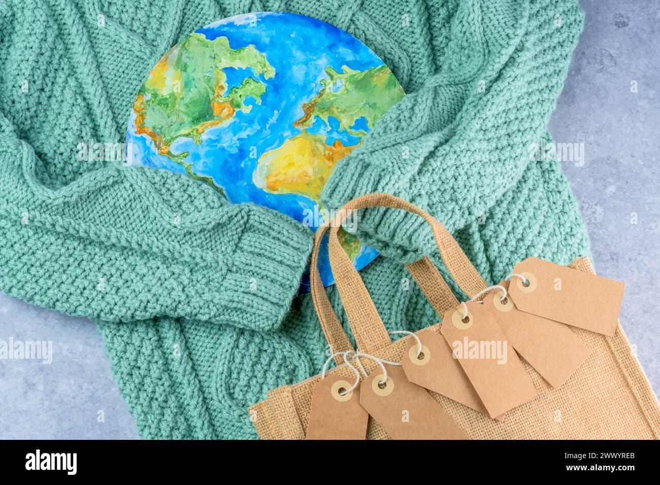 Die Pullover-Ärmel halten die Tags in der Umarmung des Planeten mit einer Öko-Tasche. Verantwortungsbewusster Konsum. Kreatives Konzept weniger kaufen Stockfoto