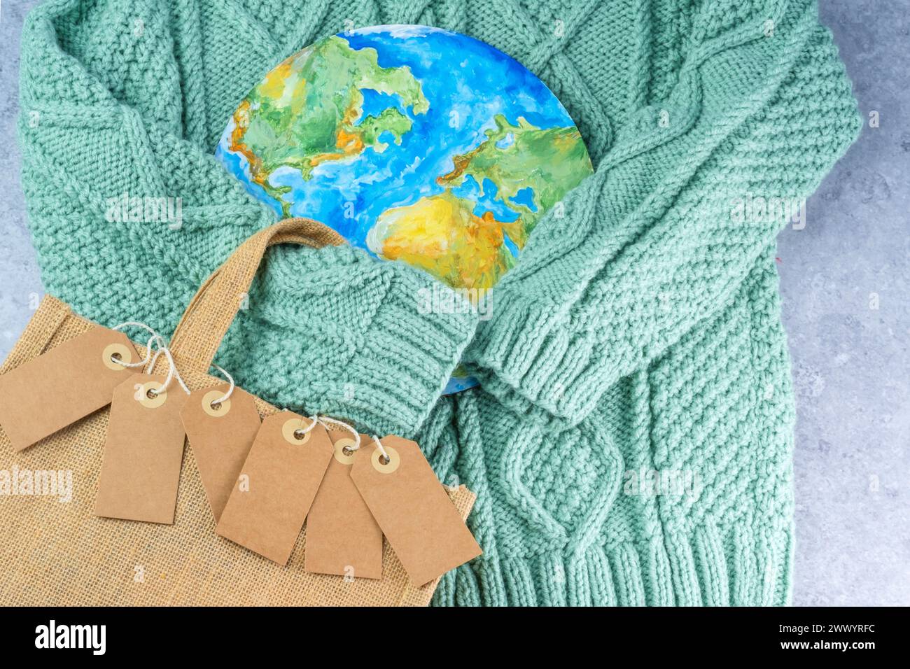 Die Pullover-Ärmel halten die Tags in der Umarmung des Planeten mit einer Öko-Tasche. Verantwortungsbewusster Konsum. Kreatives Konzept weniger kaufen Stockfoto