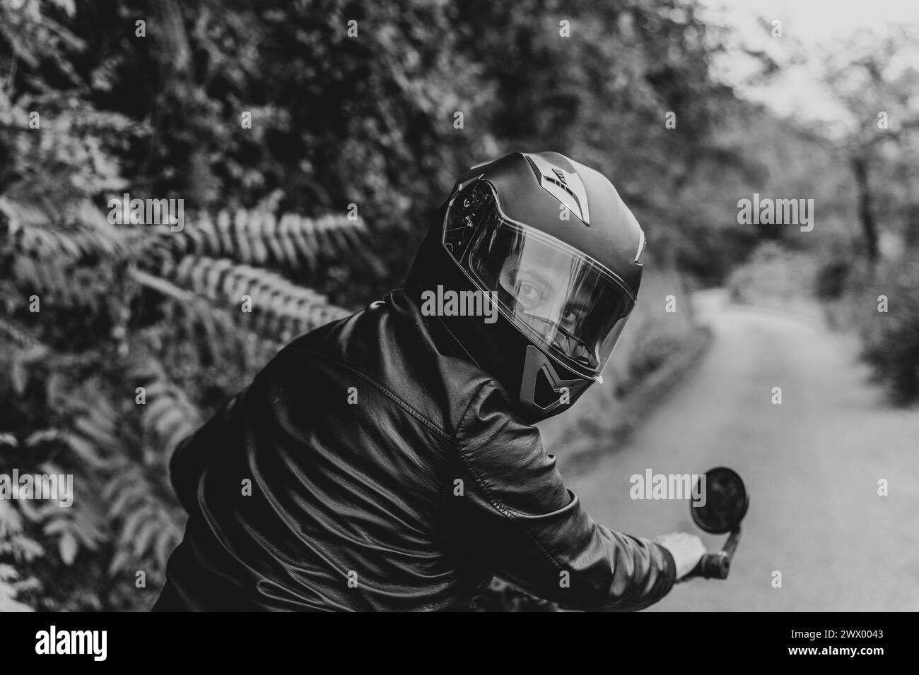 Der Blick des Fahrers. Porträt eines Mannes mit schwarzem Helm und Lederjacke, der zurückblickt. Moto-Ritt-Chroniken auf der Straße. Schwarzweiß. Stockfoto