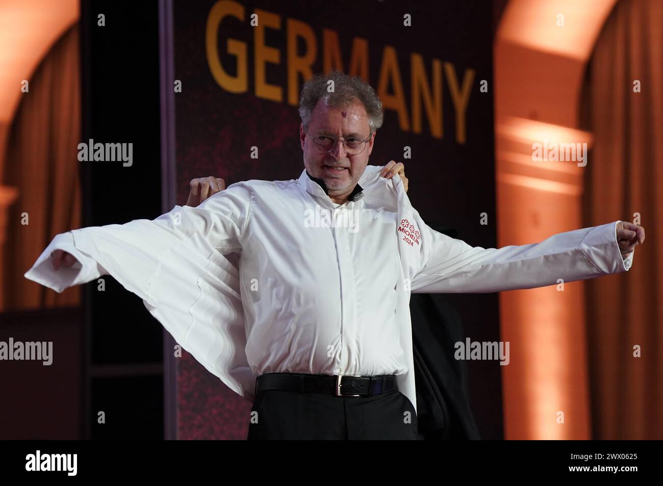 Hamburg, Deutschland. März 2024. Drei-Sterne-Koch Sven Elverfeld vom Restaurant Aqua in Wolfsburg zieht seine drei-Sterne-Küchenjacke auf die Bühne während der Preisverleihung für die Michelin-Sterne 2024 für deutsche Restaurants der Handelskammer. Der diesjährige Michelin Guide bietet 340 Restaurants, die in den letzten Monaten einen oder mehrere Sterne verdient haben, darunter zehn drei-Sterne-Restaurants. Quelle: Marcus Brandt/dpa/Alamy Live News Stockfoto