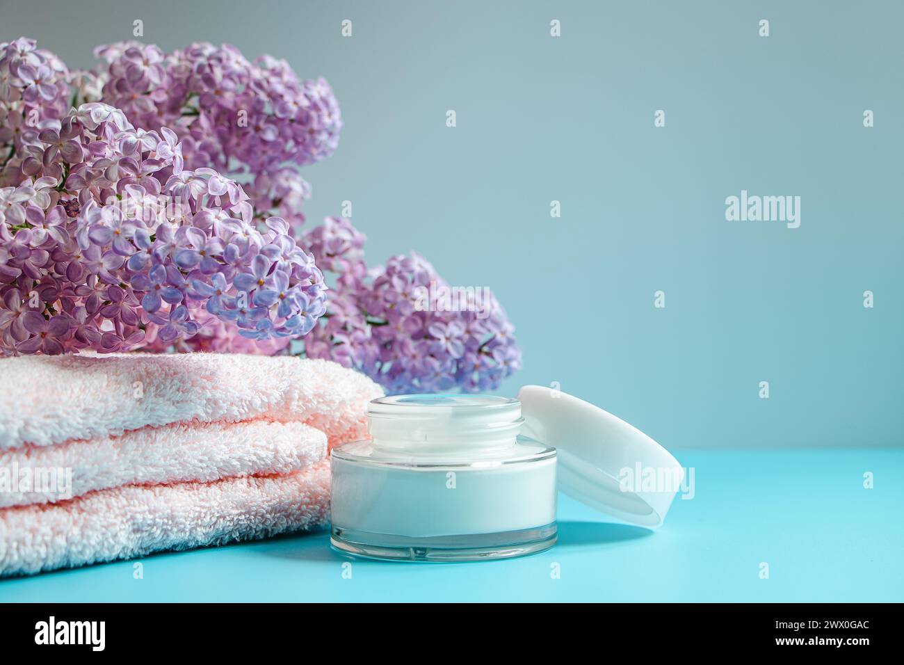 Spa- und Hautpflegekonzept. Handtuch, Creme und Seife auf dem Hintergrund zarter Fliederblüten. Stockfoto