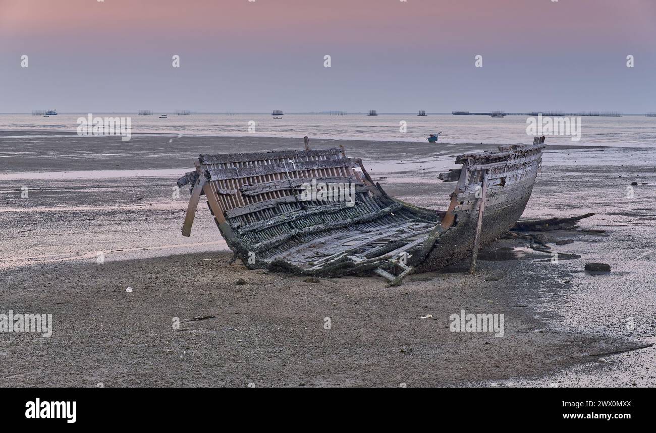 Skelett eines verlassenen Holzfischbootes, das bei Ebbe in der Abenddämmerung auf dem Sand in Pattaya, Thailand, liegt Stockfoto