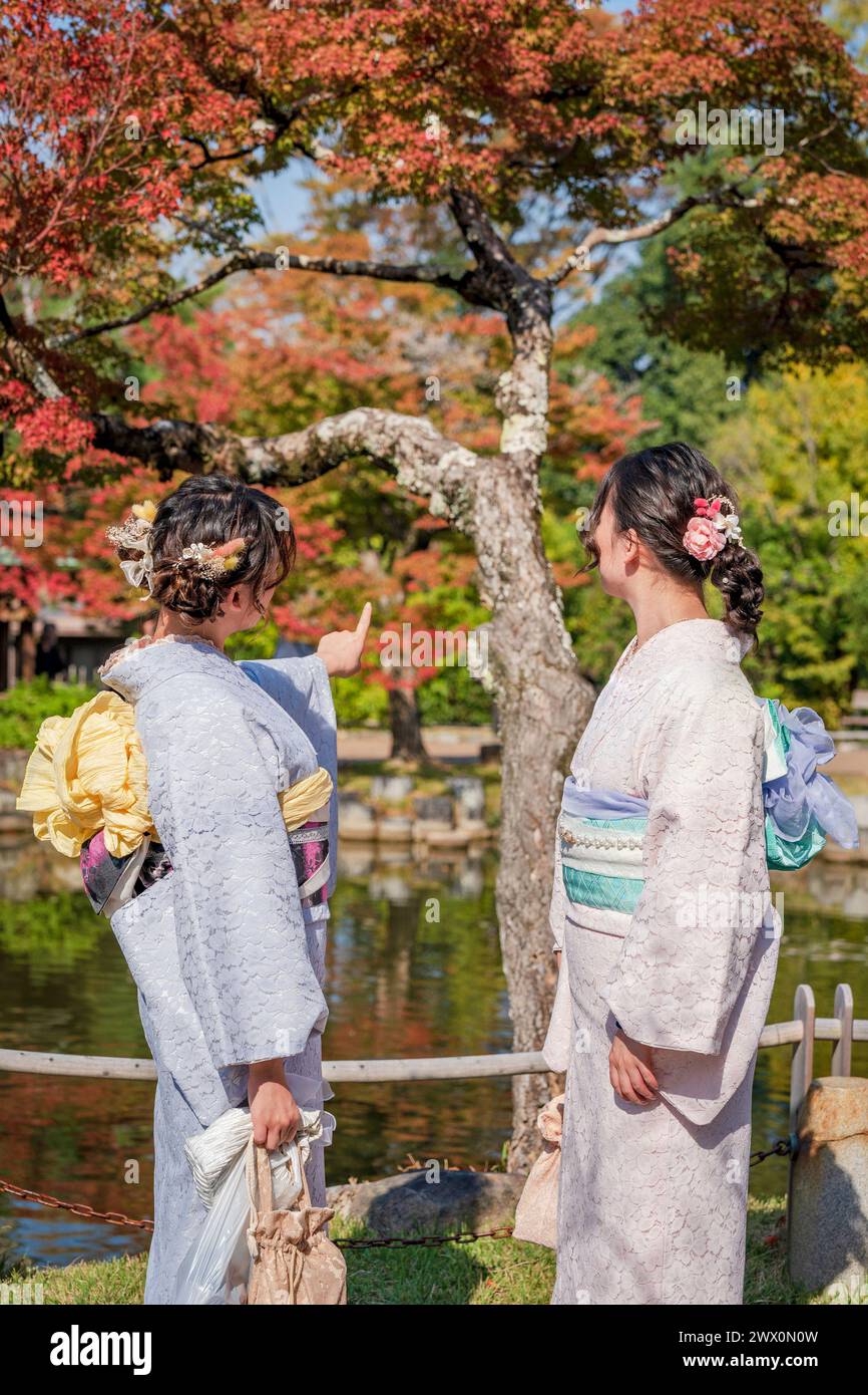Zwei Mädchen stehen vor einem Teich mit Bäumen im Hintergrund. Stockfoto