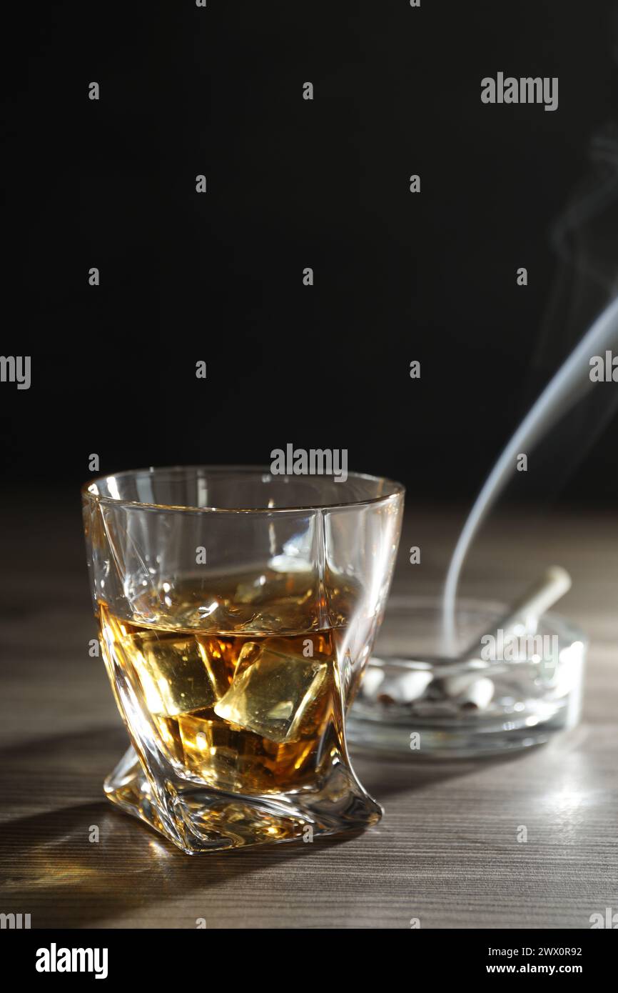 Alkoholsucht. Whiskey in Glas, Zigaretten und Aschenbecher auf Holztisch Stockfoto