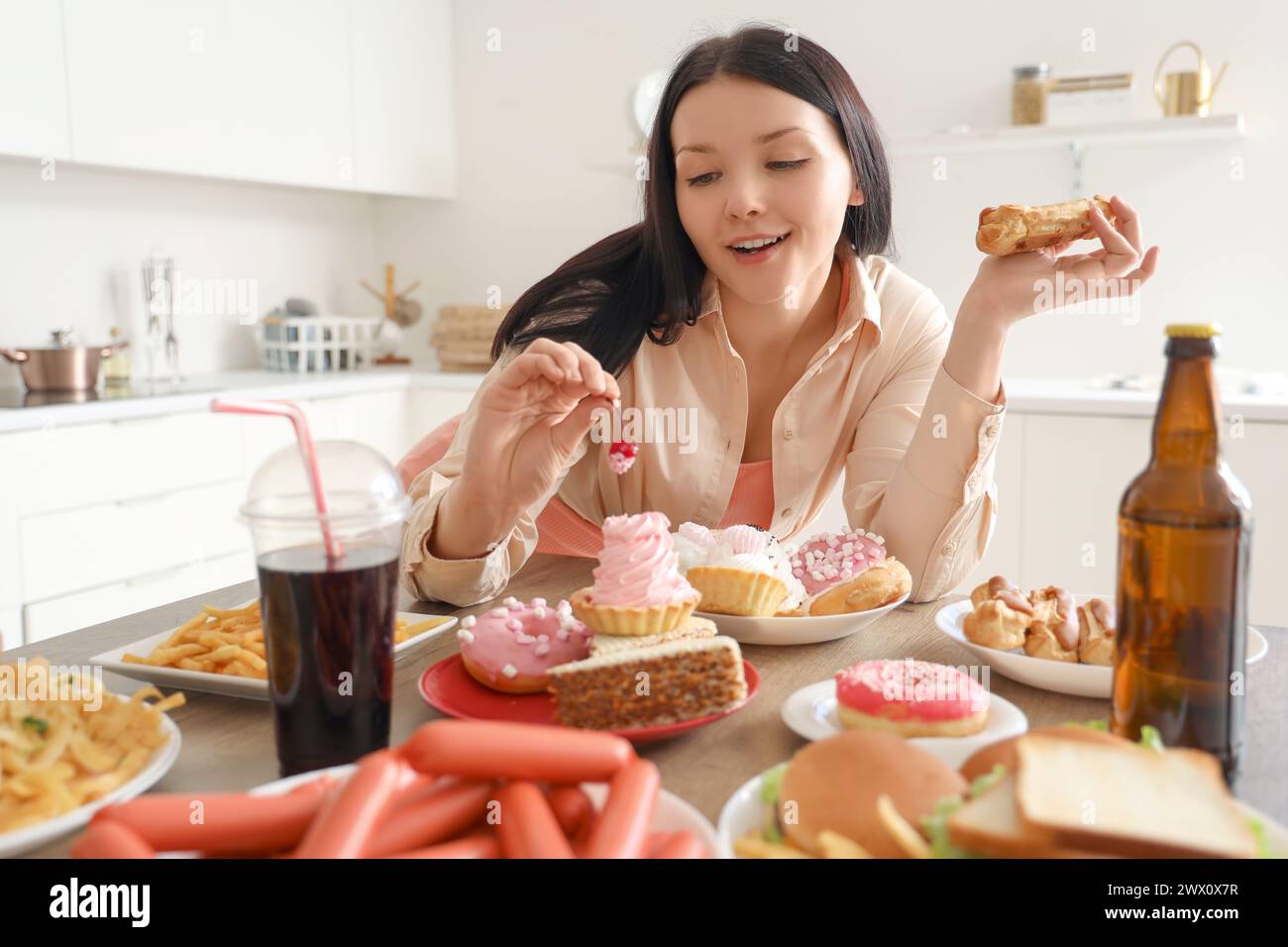 Junge Frau am Tisch mit ungesundem Essen in der Küche. Das Konzept des Überessens Stockfoto