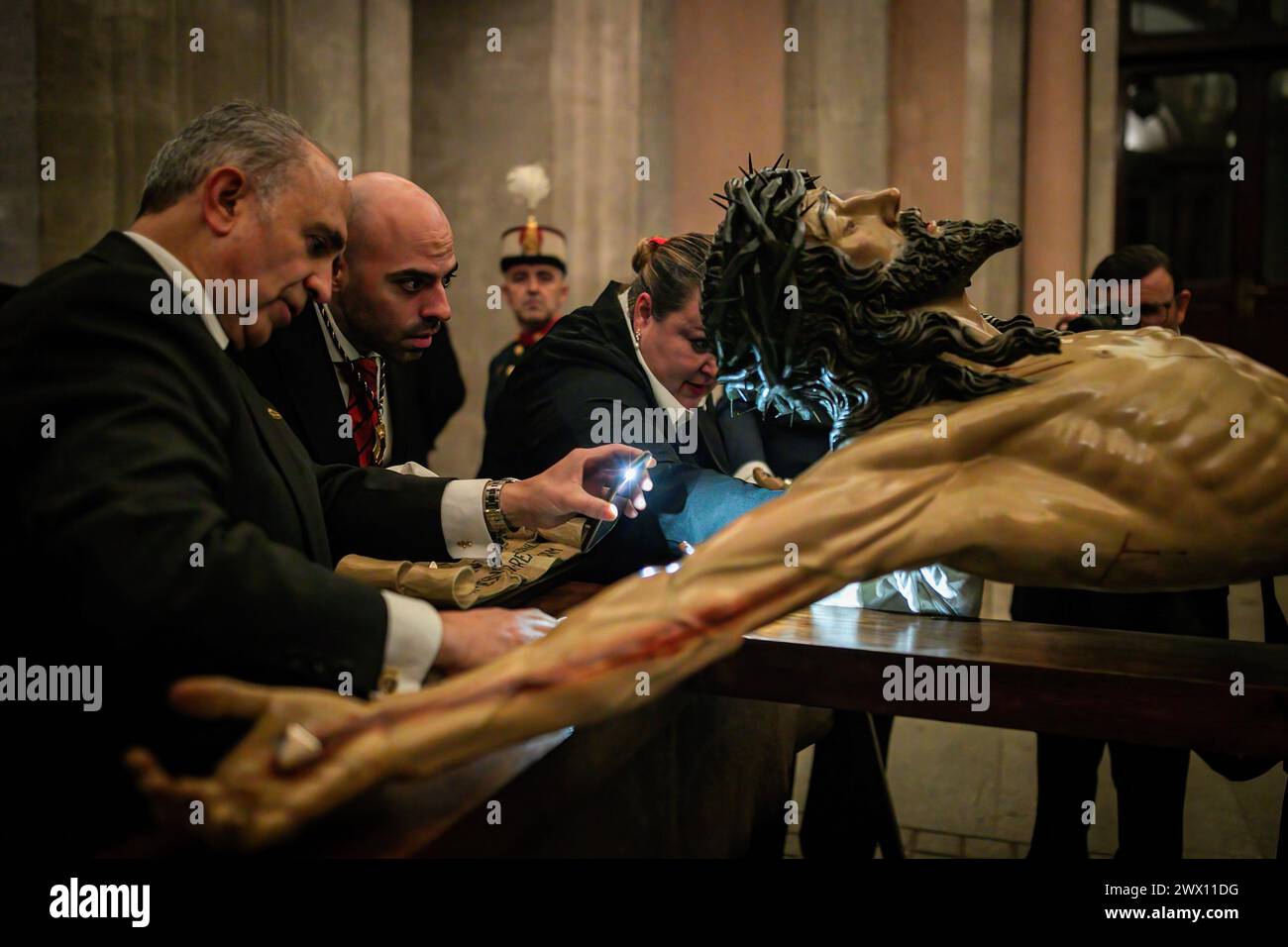 Madrid, Spanien. März 2024. Ein Bruder strahlt das Licht mit seinem Handy, während sie ihn vor dem Regen reinigen und trocknen, bei seiner Ankunft im Königlichen Palast von Madrid. An diesem Heiligen Dienstag, der von Regen bedroht ist und die Gefahr besteht, dass das Santísimo Cristo de la Fe, im Volksmund Cristo de los Alabarderos genannt, von der Militärkirche von Madrid bis zum Königspalast verarbeitet wird. (Foto: David Canales/SOPA Images/SIPA USA) Credit: SIPA USA/Alamy Live News Stockfoto