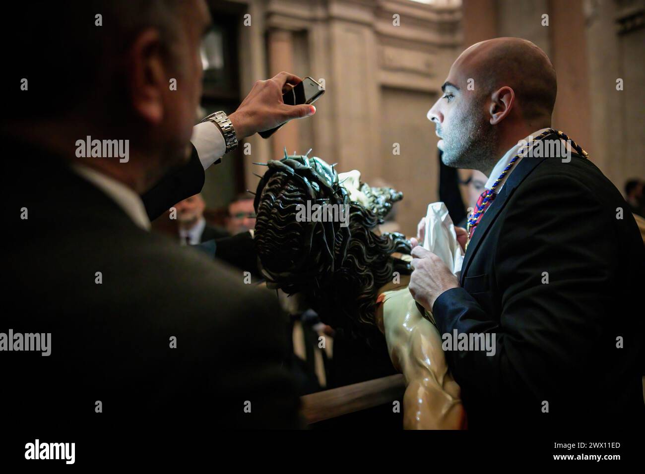 Madrid, Spanien. März 2024. Ein Bruder beobachtet mit einem Tuch in der Hand den Santísimo Cristo de la Fe, im Volksmund Cristo de los Alabarderos genannt, während ein anderer Bruder das Licht mit seinem Handy strahlt. An diesem Heiligen Dienstag, der von Regen bedroht ist und die Gefahr besteht, dass das Santísimo Cristo de la Fe, im Volksmund Cristo de los Alabarderos genannt, von der Militärkirche von Madrid bis zum Königspalast verarbeitet wird. (Foto: David Canales/SOPA Images/SIPA USA) Credit: SIPA USA/Alamy Live News Stockfoto