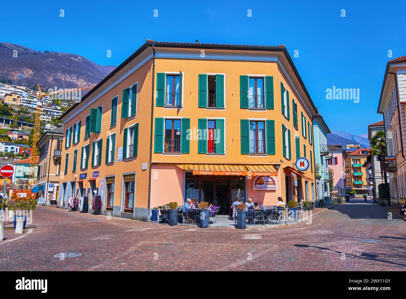 LOCARNO, SCHWEIZ - 26. MÄRZ 2022: Piazza di San Francesco mit alten Häusern, Restaurants im Freien und Bergen, im Hintergrund gesehen, Locarno, SW Stockfoto