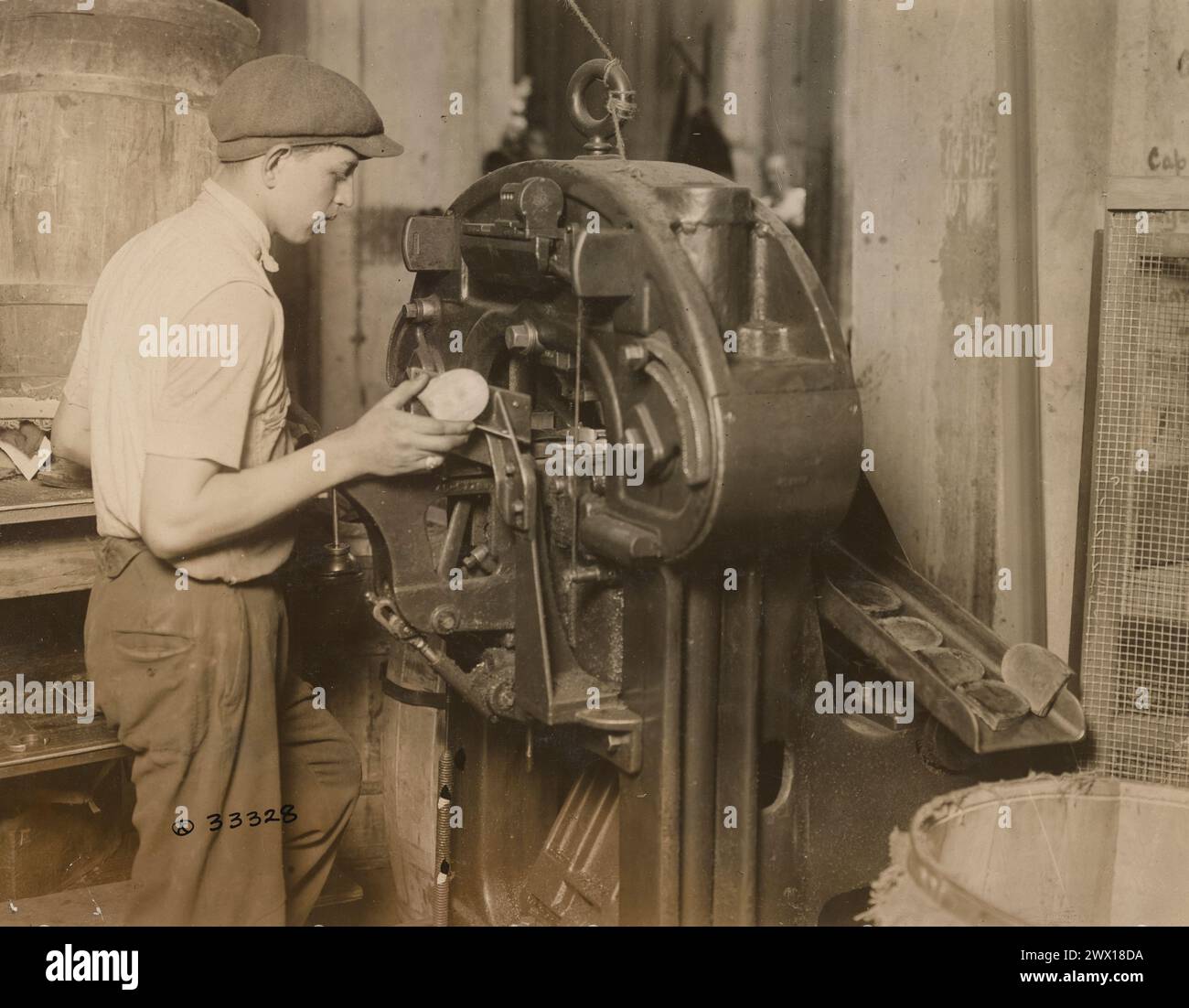 Herstellung von Schuhen der US-Armee – Mann, der eine Maschine bedient, die fünf Tonnen hydraulischen Druck auf die montierten Fersen ausübt, um sie richtig zusammenzudrücken und in Form zu Formen. Rosenwasser and Brothers Inc., Long Island City, New York CA. 1918 Stockfoto