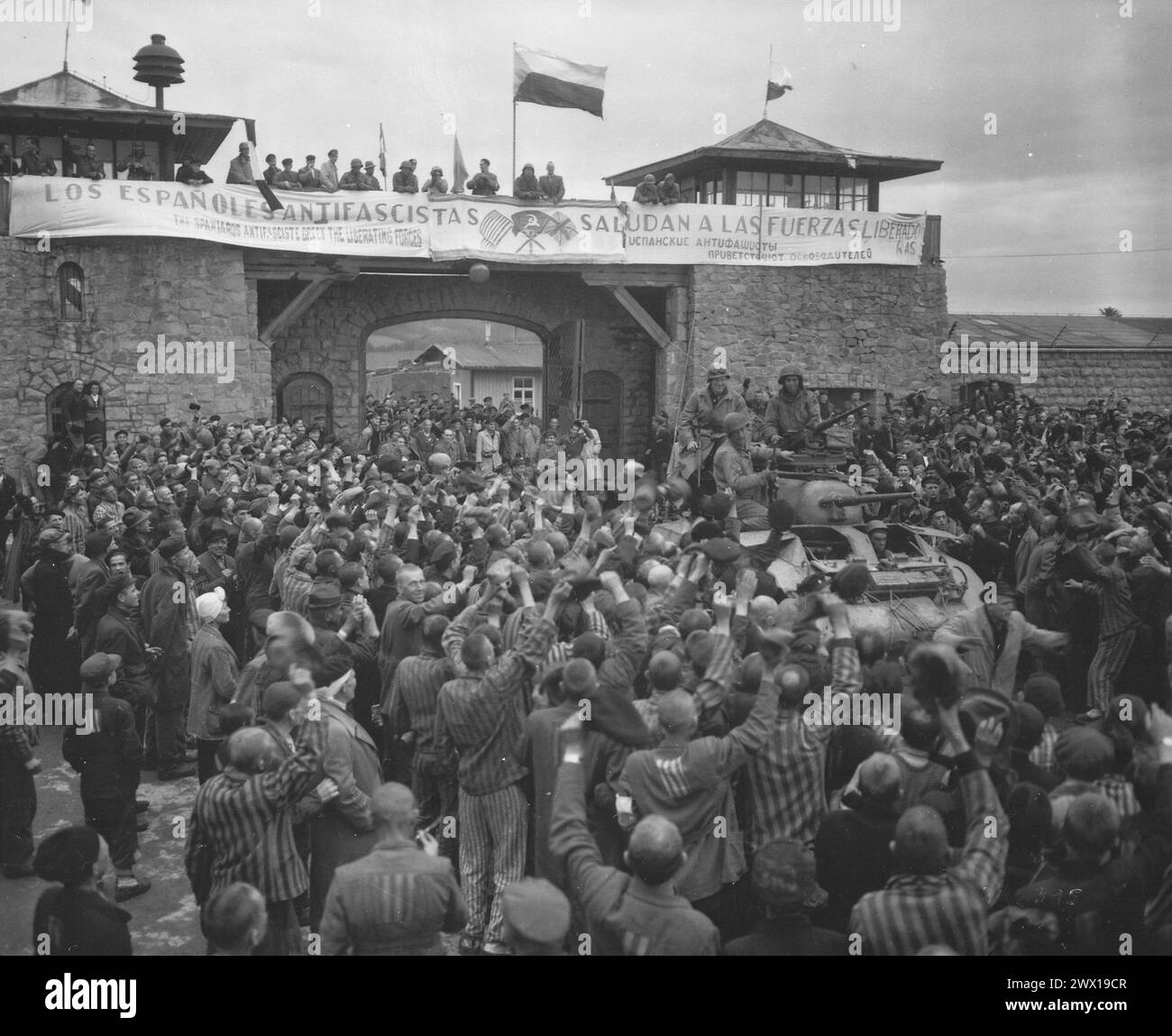Befreite Gefangene im Konzentrationslager Mauthausen bei Linz, Österreich, heißen Kavalleristen der 11. Panzerdivision willkommen. Das Banner über der Mauer wurde von spanischen Loyalisten-Gefangenen CA. Mai 1945 Stockfoto