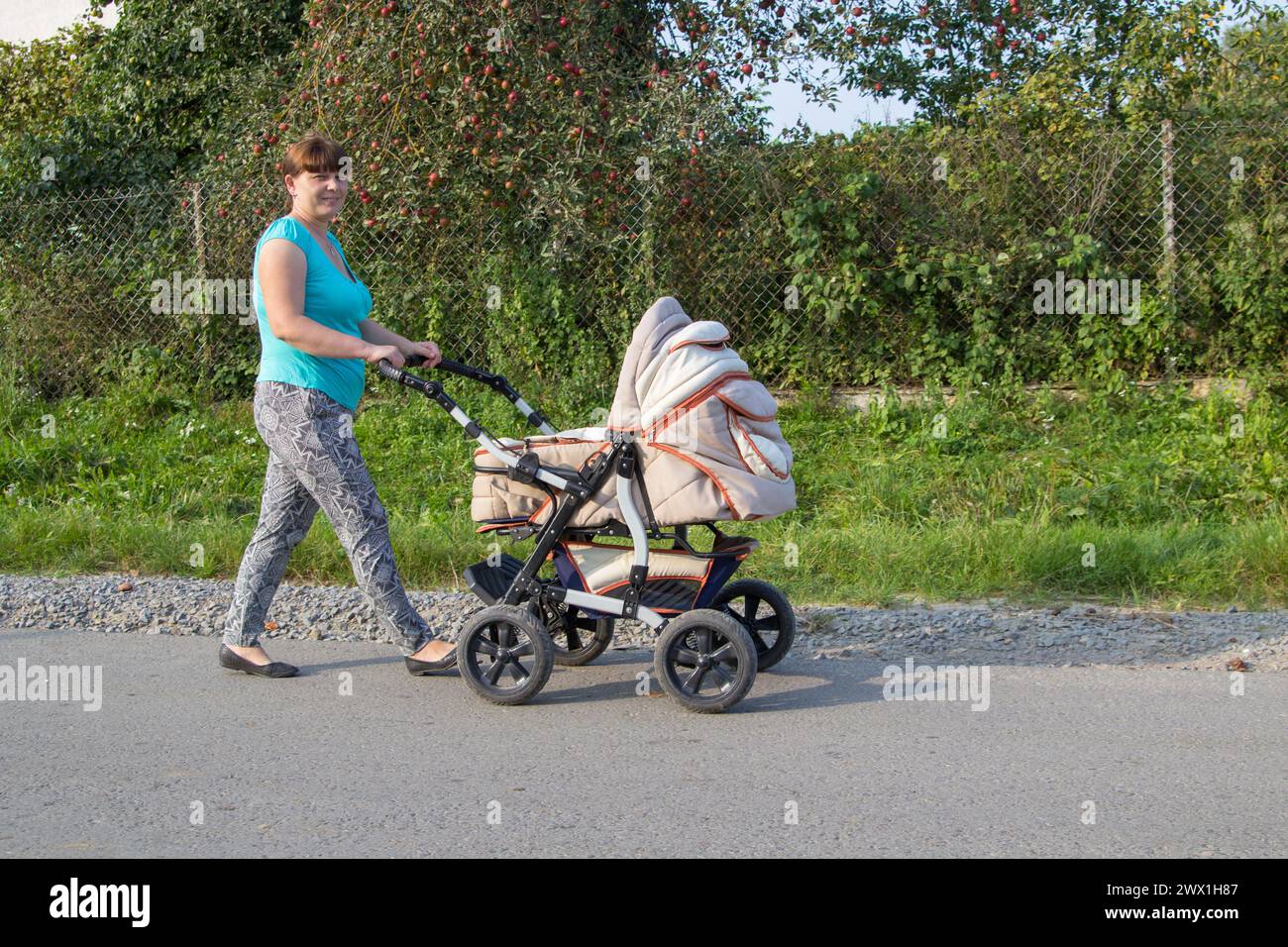 Glückliche Mutter, die einen Kinderwagen fährt, ein neugeborenes Baby im Sommer auf der Straße Stockfoto