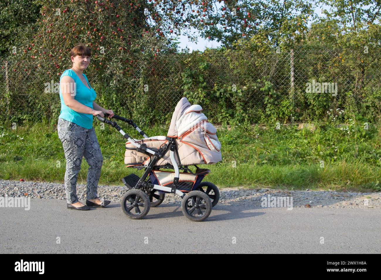 Auf der Straße fährt Asphalt eine Frau mit Kinderwagen ein neugeborenes Baby, ein Apfelrot mit Kinderwagen Stockfoto