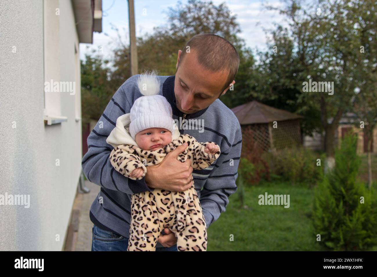 Der Vater sieht das Baby in seinen Armen an, das Baby ist unglücklich Stockfoto
