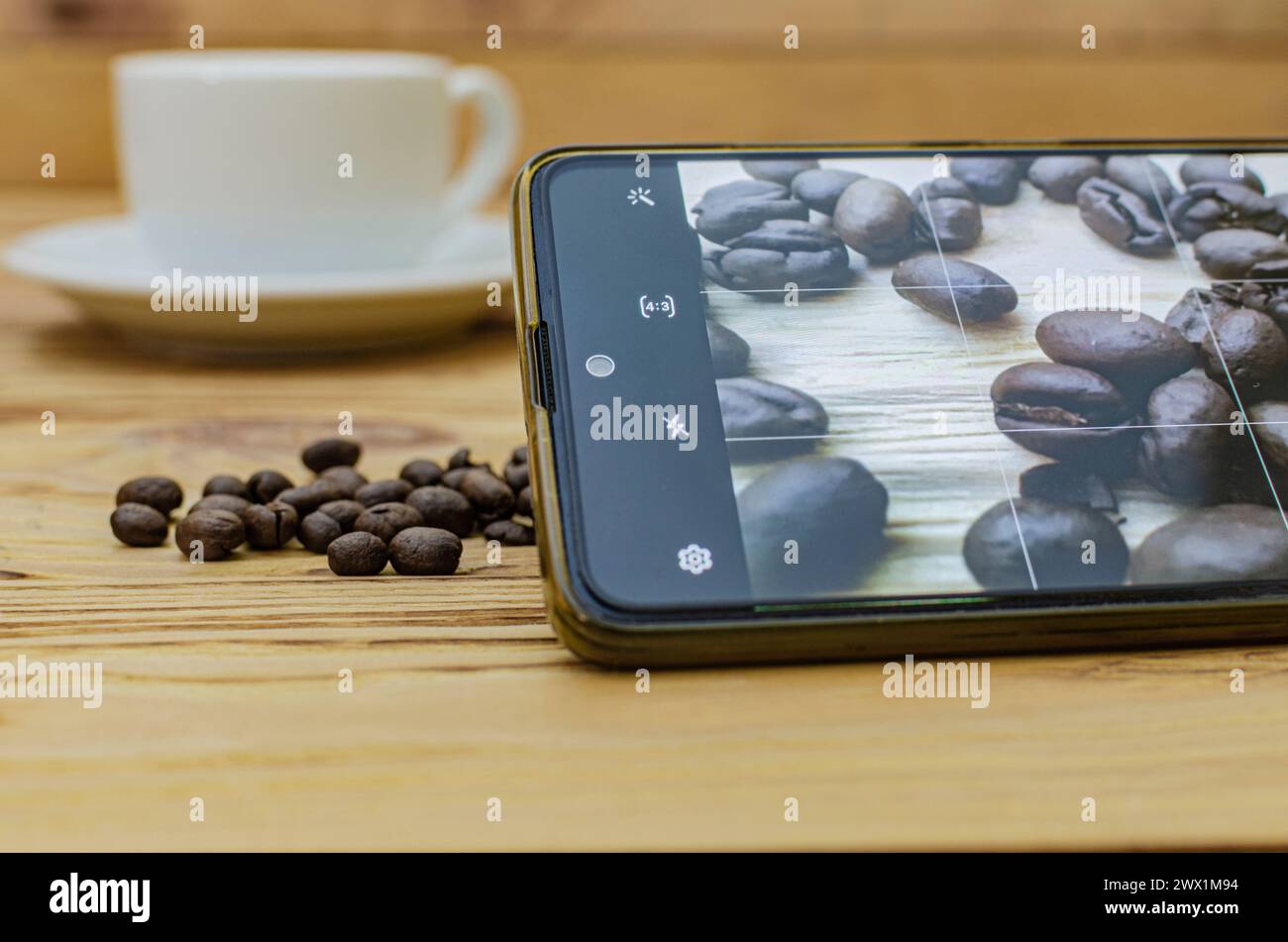 Nahaufnahme eines Smartphones, das ein Foto verschütteter Kaffeebohnen auf einem Tisch in einem Café macht Stockfoto