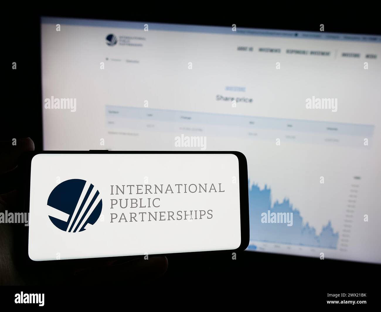 Person, die ein Mobiltelefon mit dem Logo des britischen Unternehmens International Public Partnerships Limited vor der Webseite hält. Schwerpunkt auf dem Display des Telefons. Stockfoto