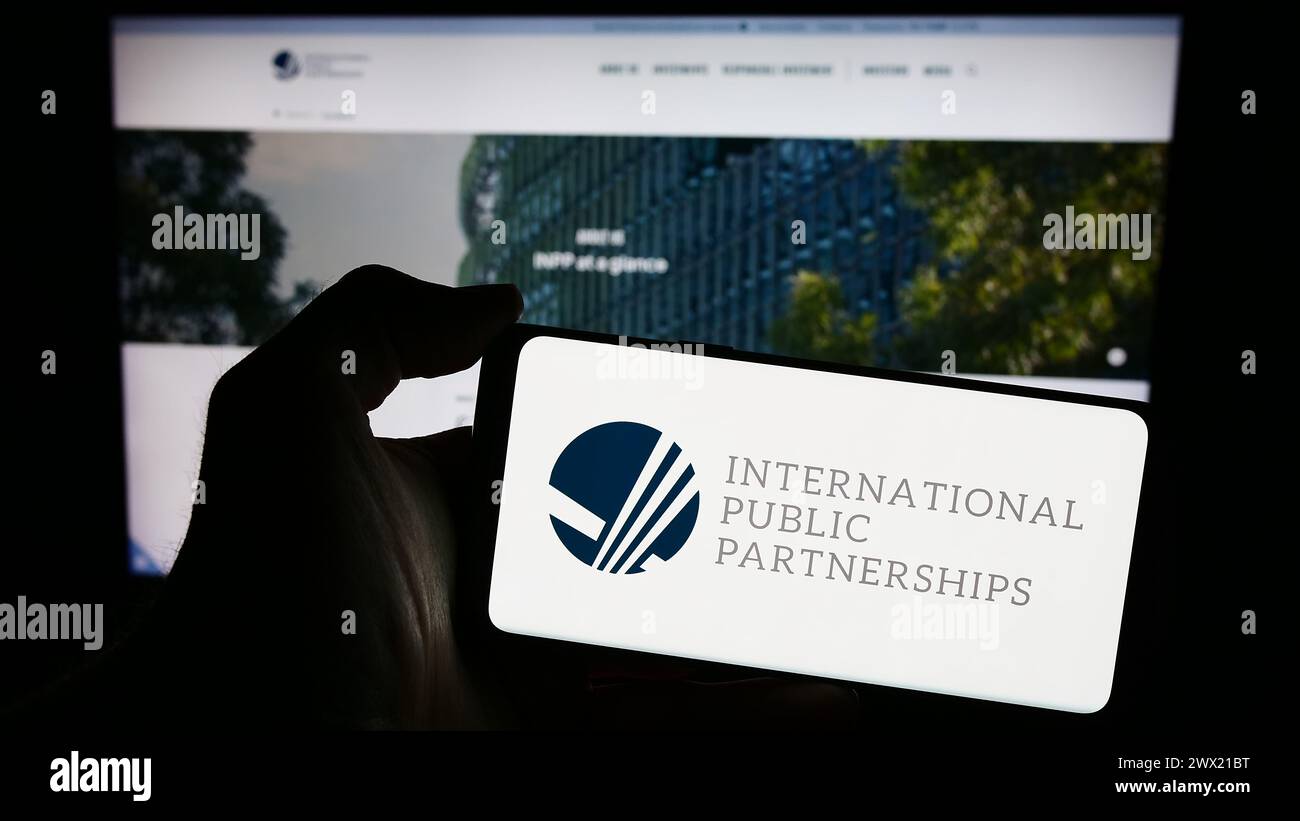 Person mit Smartphone und Logo des britischen Unternehmens International Public Partnerships Limited vor der Website. Schwerpunkt auf dem Display des Telefons. Stockfoto