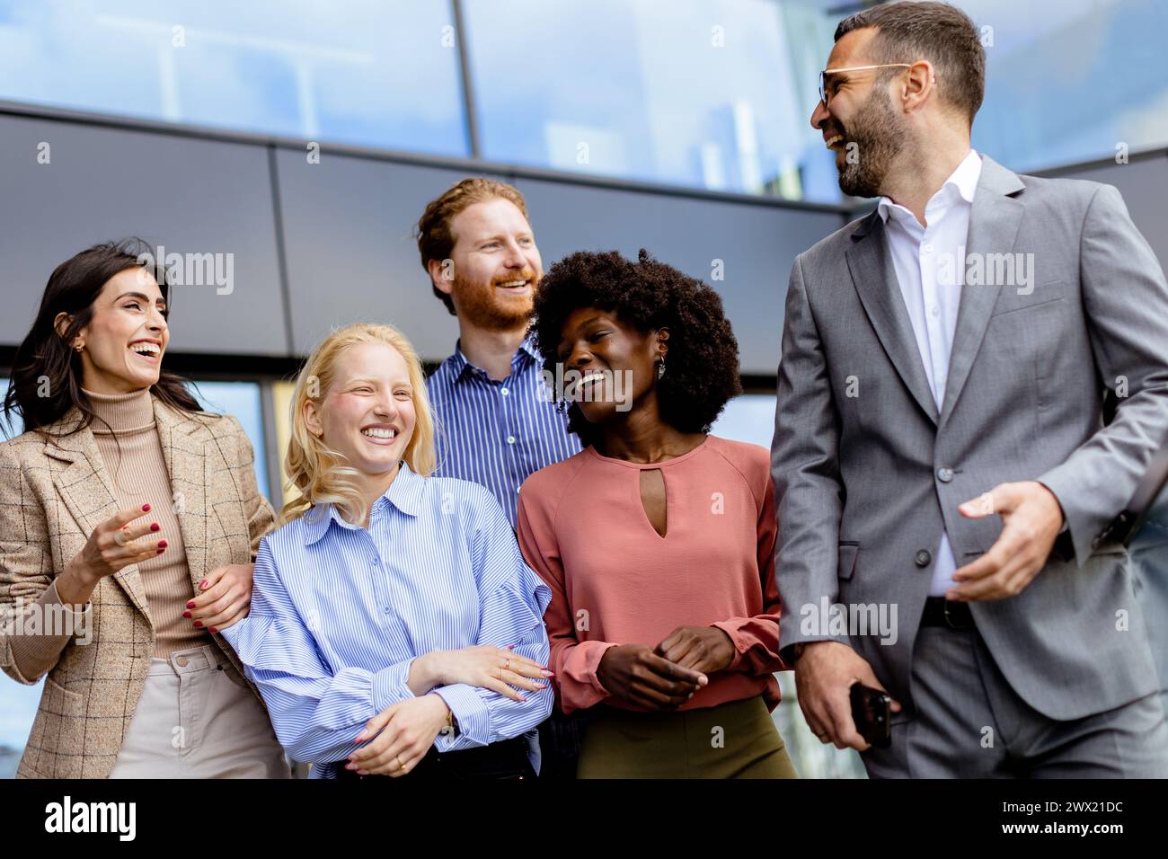 Eine Gruppe geschäftiger Mitarbeiter versammelt sich zu einem zwanglosen Gespräch vor einem modernen Büro, das Teamarbeit und Verbundenheit widerspiegelt. Stockfoto