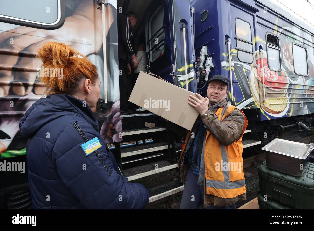 CHARKIW, UKRAINE - 26. MÄRZ 2024 - Freiwillige und Mitarbeiter der ukrainischen Roten Kreuz-Gesellschaft erhalten Mittagessen für Patienten von Krankenhäusern und Binnenvertriebenen, die in Herbergen des Food Train leben, die in der Stadt angekommen sind und an Stromausfällen leiden, die durch russische Angriffe auf kritische Infrastrukturen verursacht wurden; Charkiw, Nordost-Ukraine. Der Food Train ist ein Projekt der Ukrainischen Eisenbahn (Ukrzaliznytsia), das mit der Gründung des US-amerikanischen Milliardärs Howard Buffett umgesetzt wurde. Der Küchenzug kann mehr als 10.000 Portionen Essen pro Tag produzieren, selbst wenn es keinen Strom gibt. Stockfoto