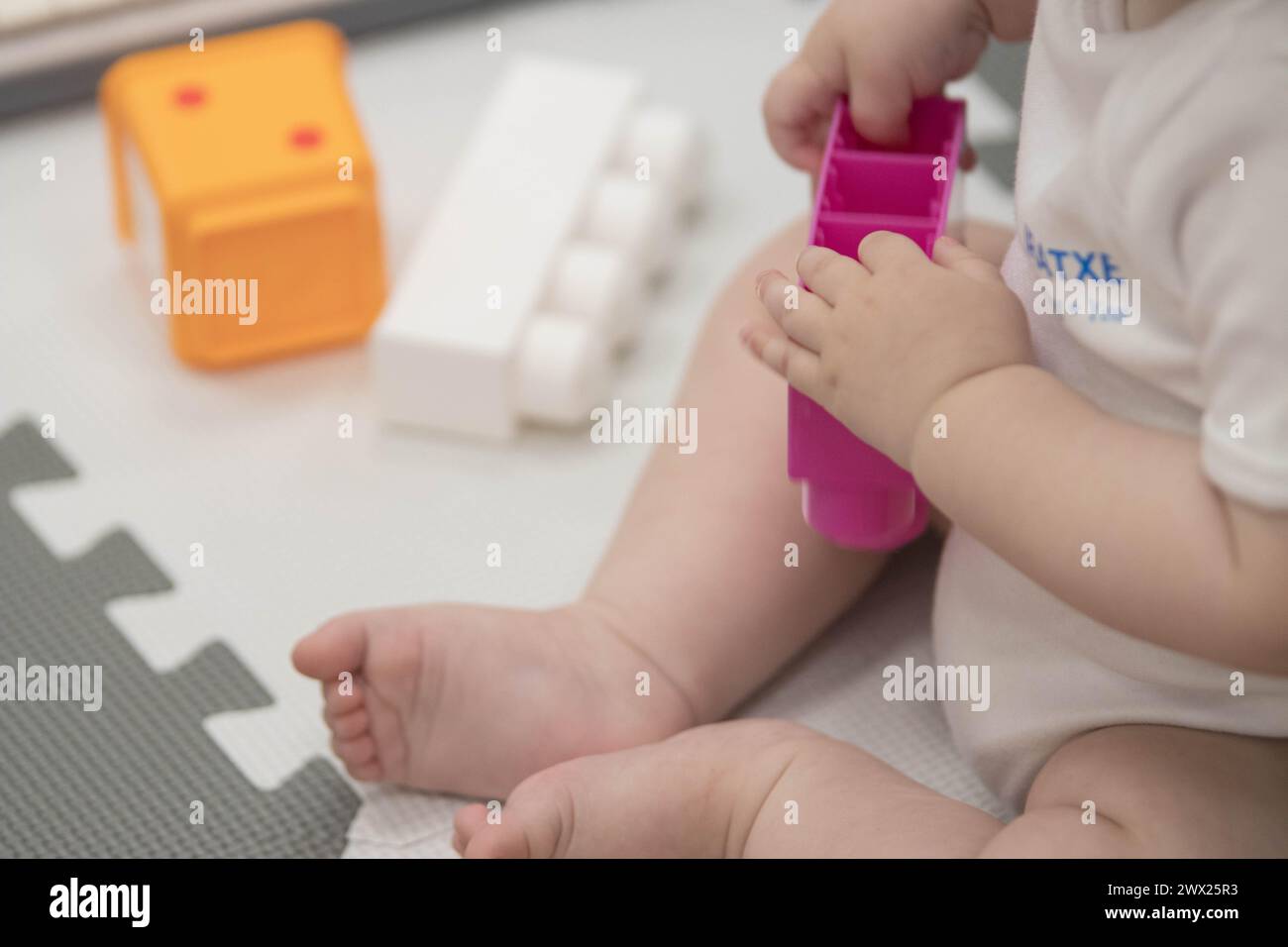 Das Kind greift während des Sitzens spielerisch mit Blöcken und anderen Spielzeugen in der Kinderbetreuung um. Enge Feldtiefe bei Nahaufnahmen der Hände des Neugeborenen Stockfoto