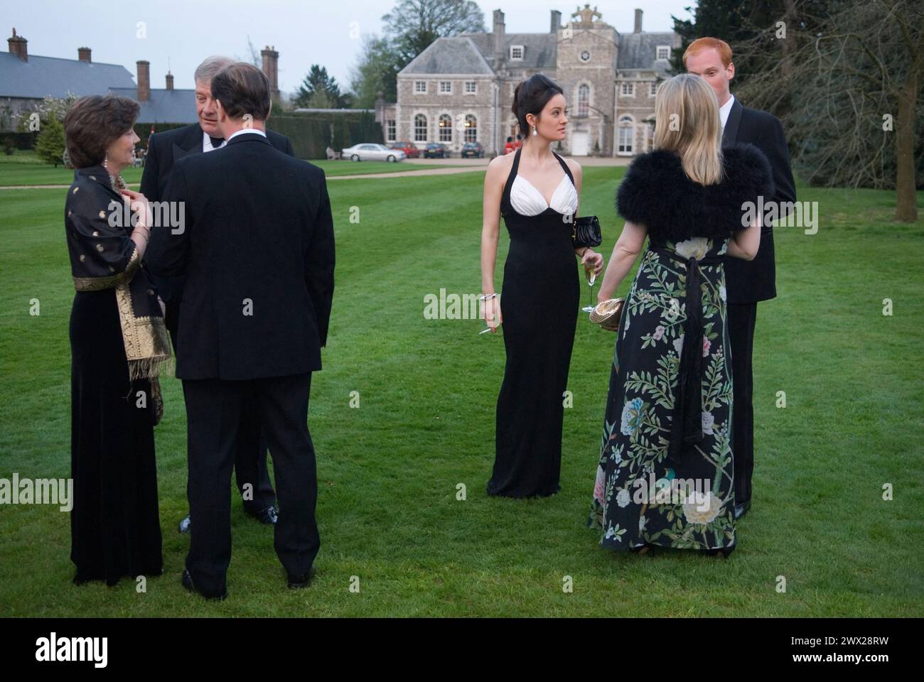 Eine junge Frau, die ein schwarz-weißes Abendkleid trägt, unter Freunden. Wohltätige Tanzgäste unterhalten sich in den Gärten, bevor sie in das Festzelt in den Gärten des Farleigh Wallop House, Farleigh Wallop, Hampshire, gehen. 2008 2000er Jahre UK HOMER SYKES Stockfoto